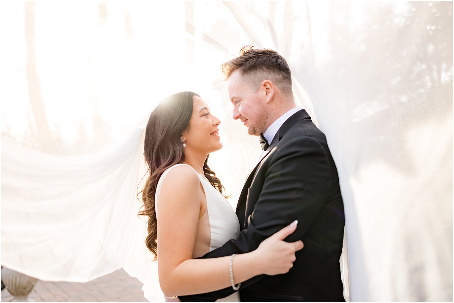 bride hugs groom under veil at sunset