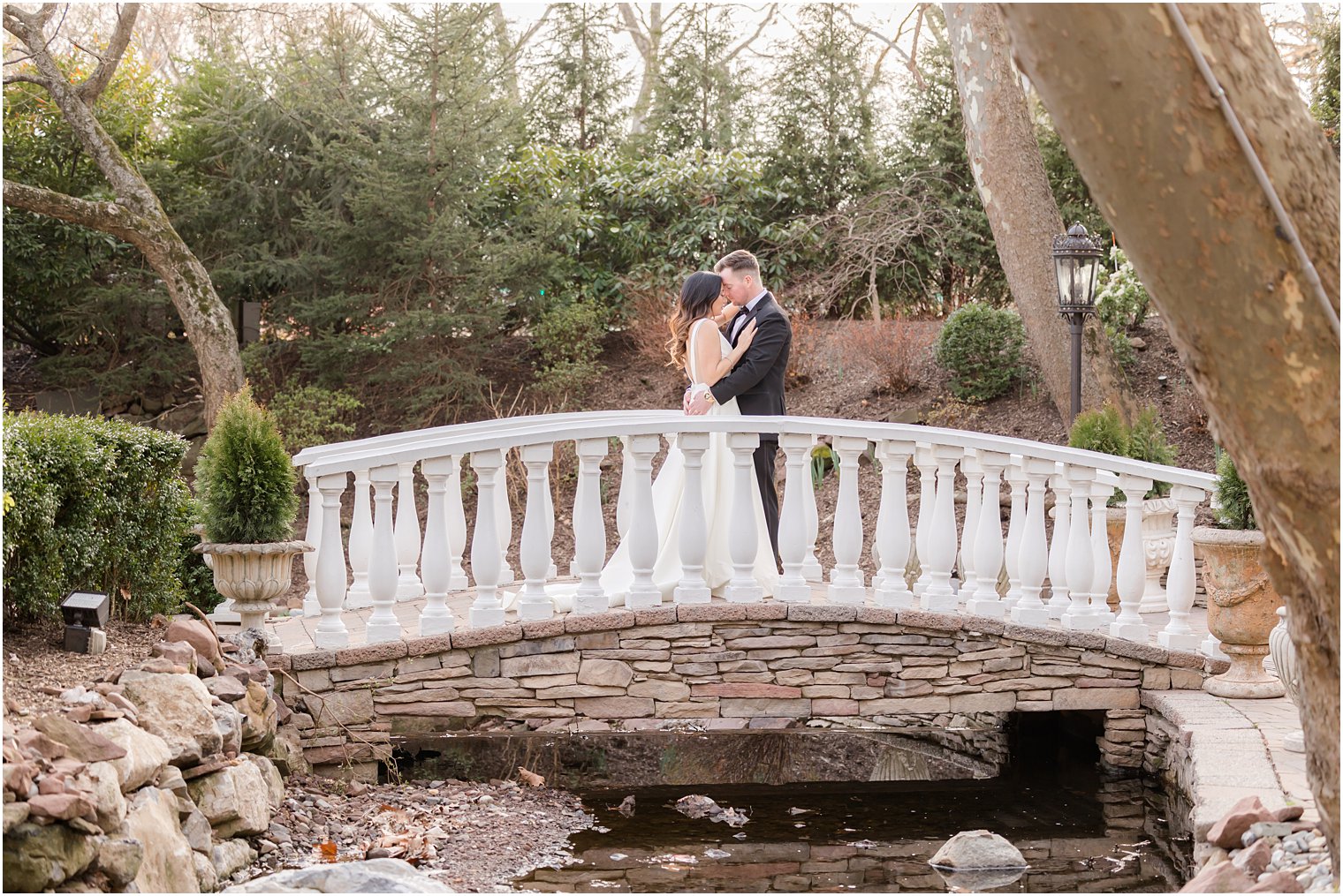 groom kisses bride's forehead on bridge in gardens at Nanina's in the Park