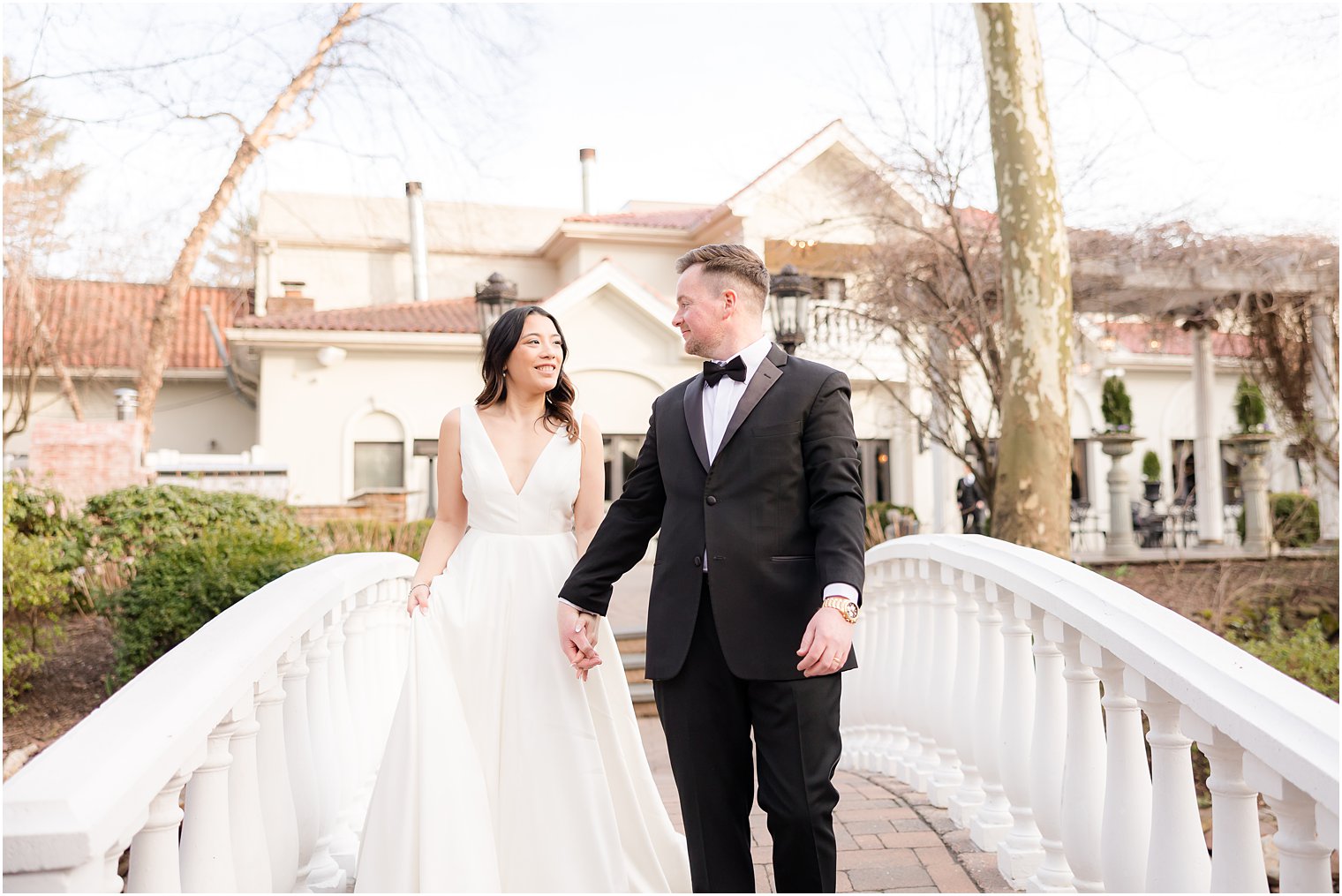 newlyweds hold hands walking over bridge at Nanina's in the Park