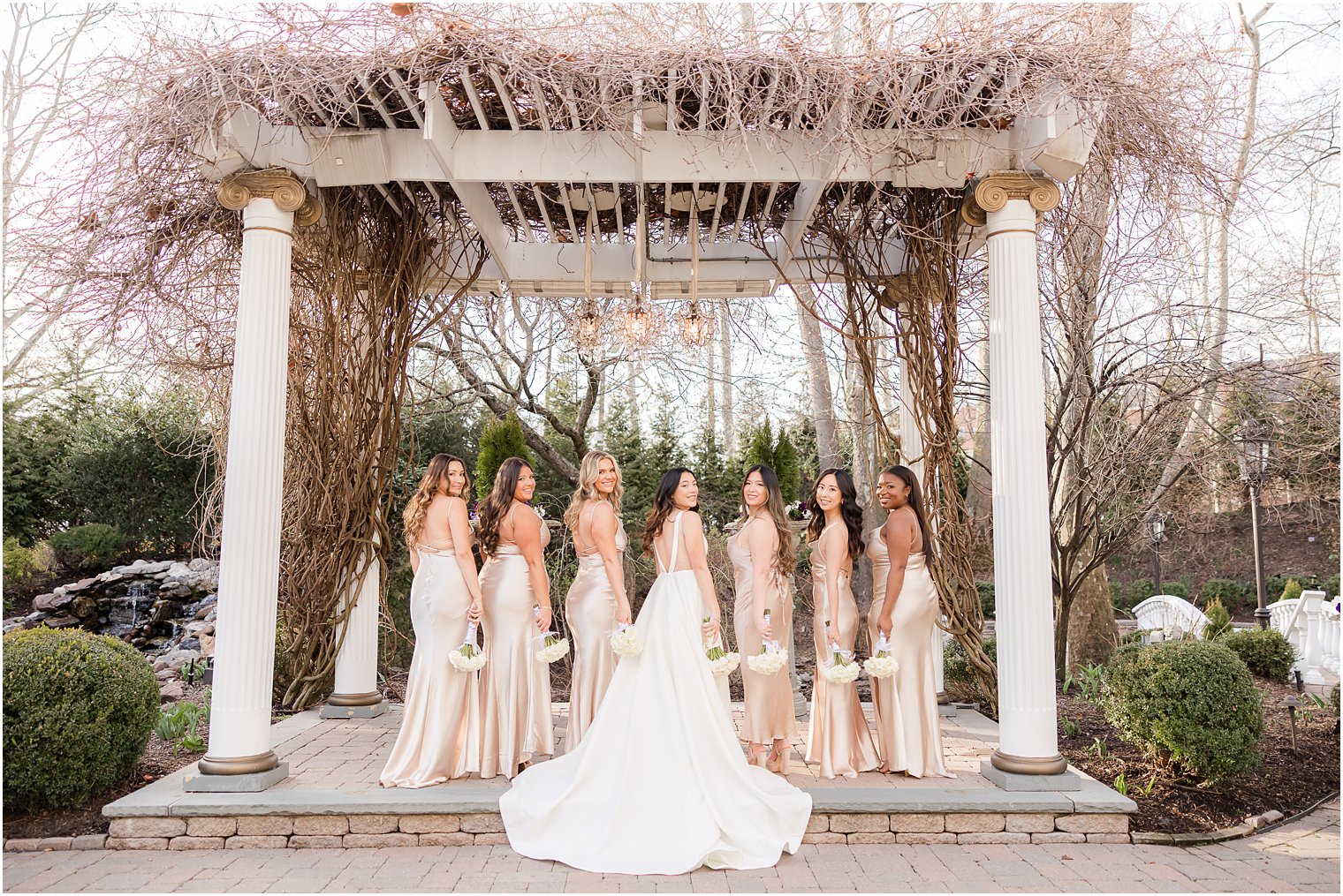bride and bridesmaids in champagne gowns pose with bouquets behind their backs 