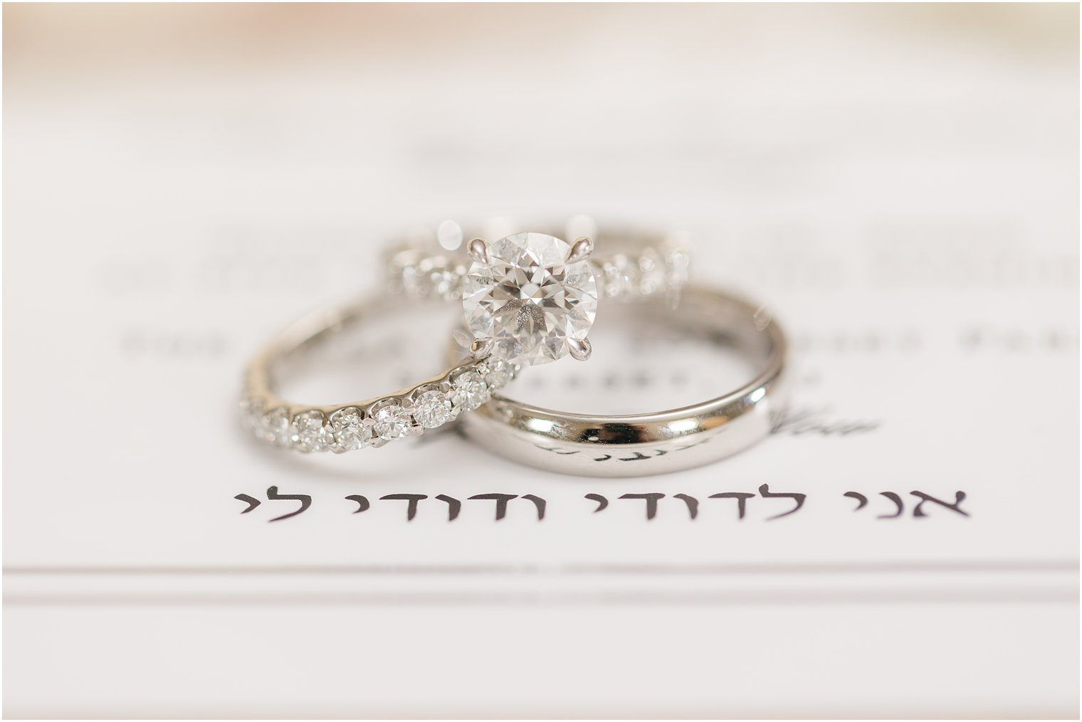 three wedding bands lay near Hebrew writing on invitation 