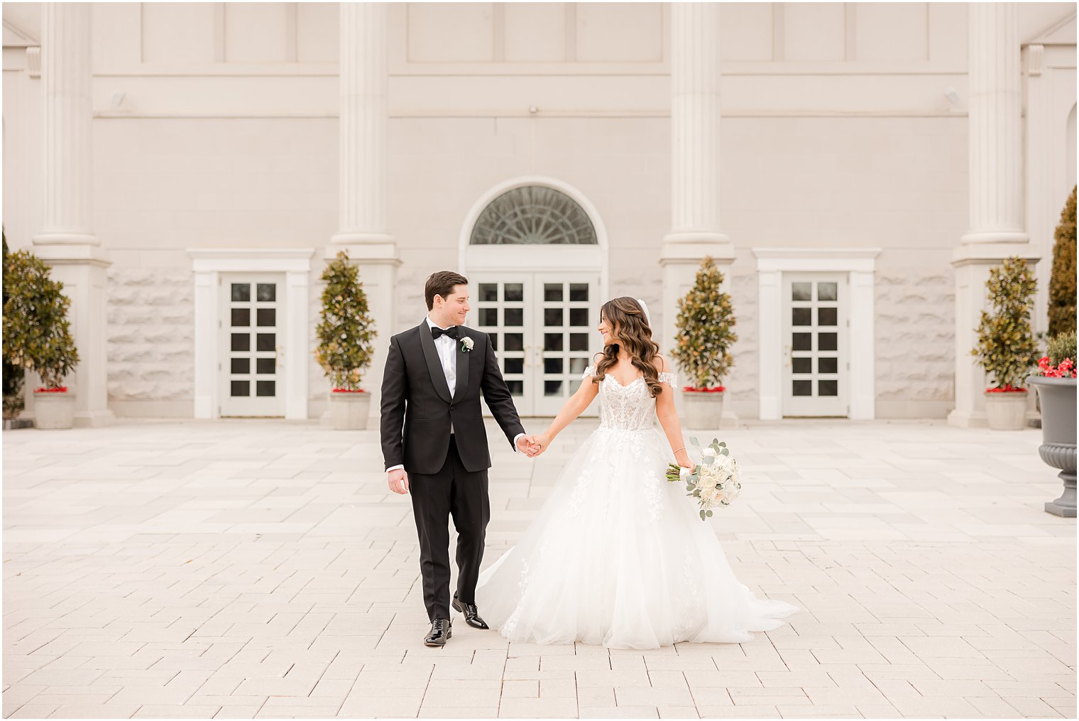 newlyweds hold hands walking on front patio at the Palace at Somerset Park