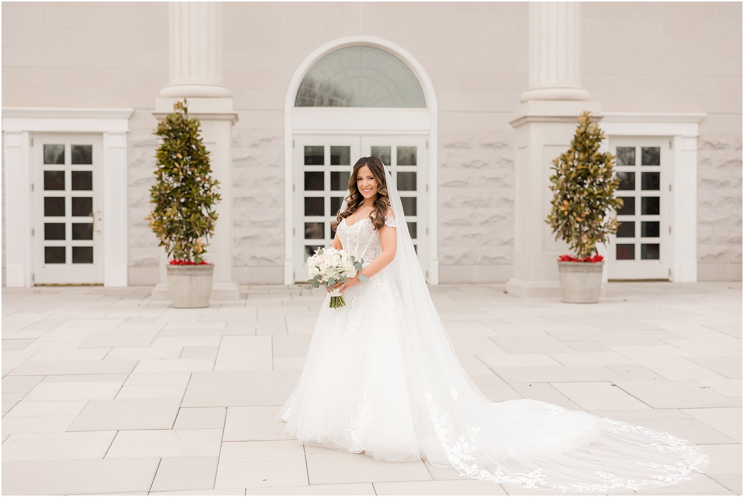 bride stands holding bouquet of ivory flowers outside the Palace at Somerset Park