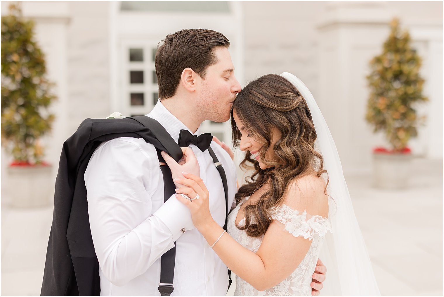groom kisses bride's head while holding his jacket over his shoulder 
