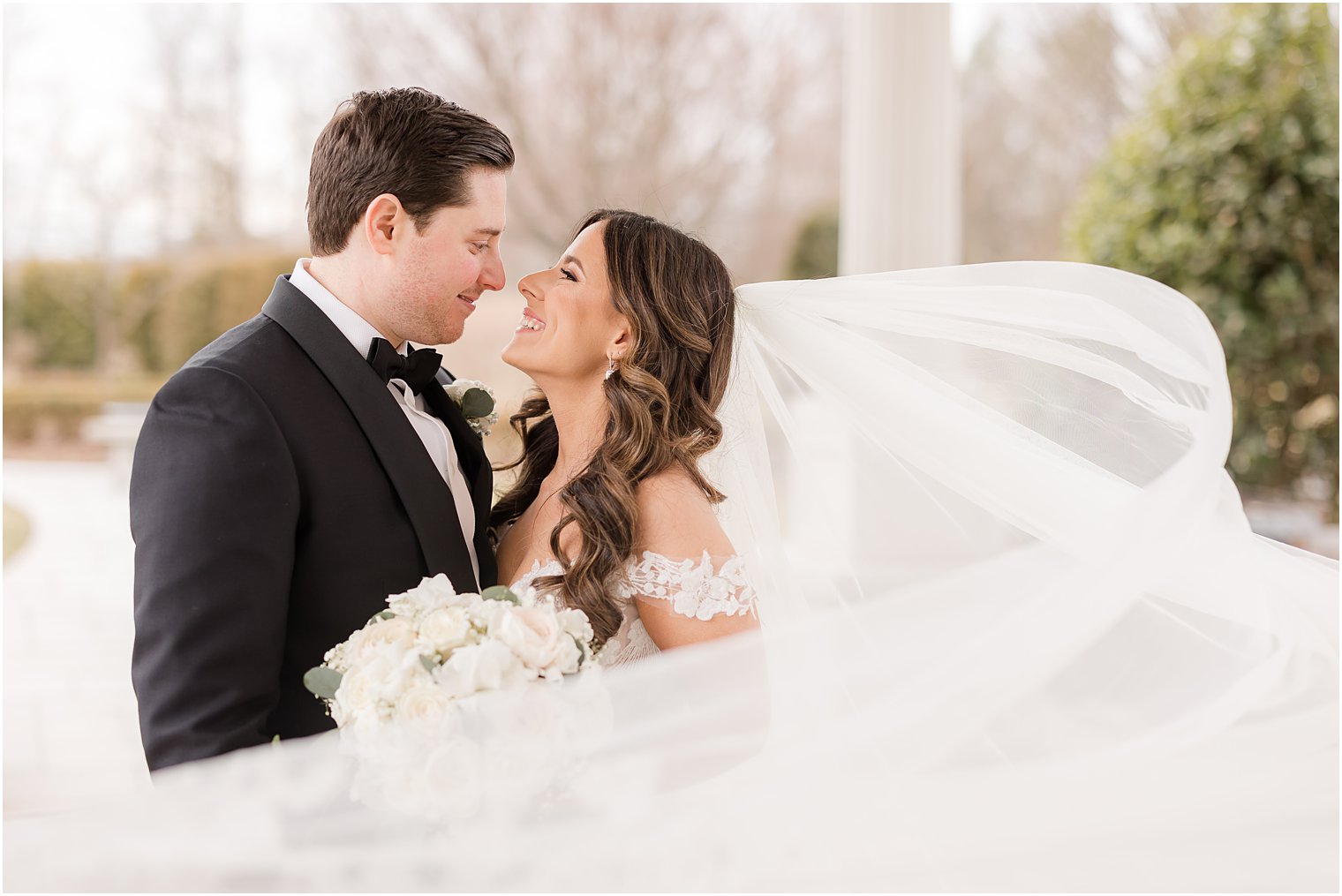 bride and groom lean together touching noses with veil around them 