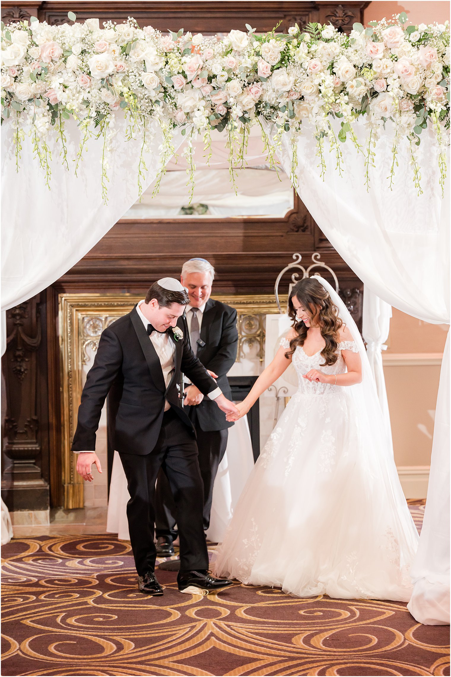 groom breaks glass holding bride's hand during traditional Jewish wedding at the Palace at Somerset Park