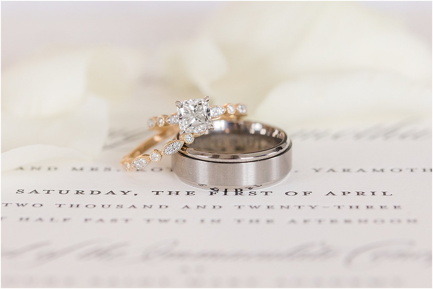 wedding bands rest on invitation suite with ivory flowers 