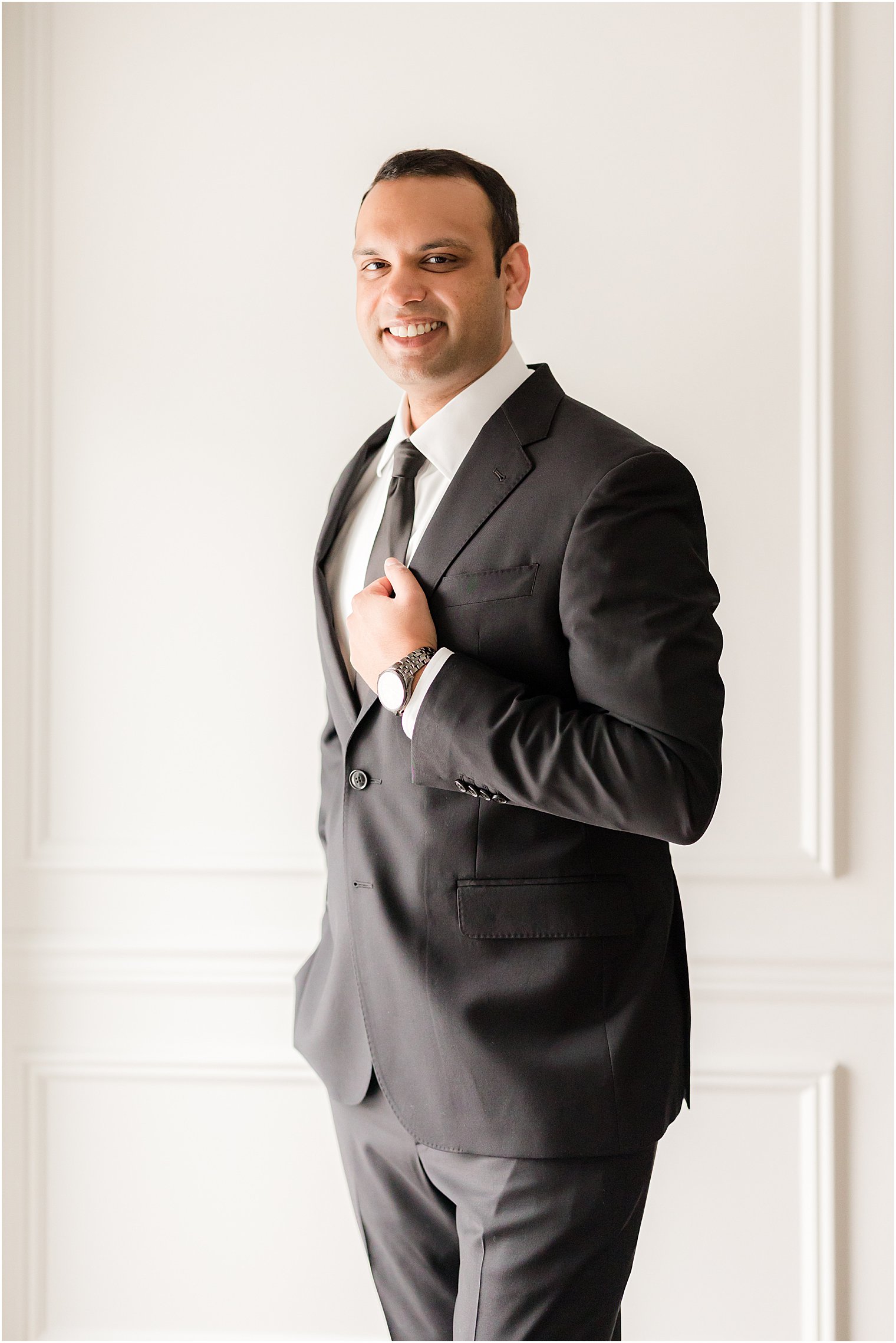 groom adjusts lapel on black suit 