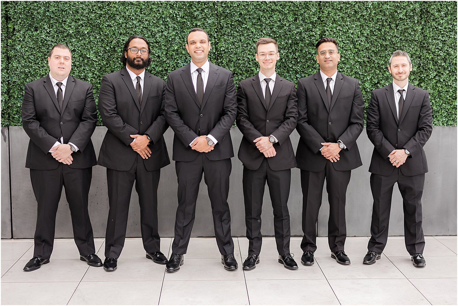groom stands with groomsmen by greenery wall Mount Saint Mary Academy