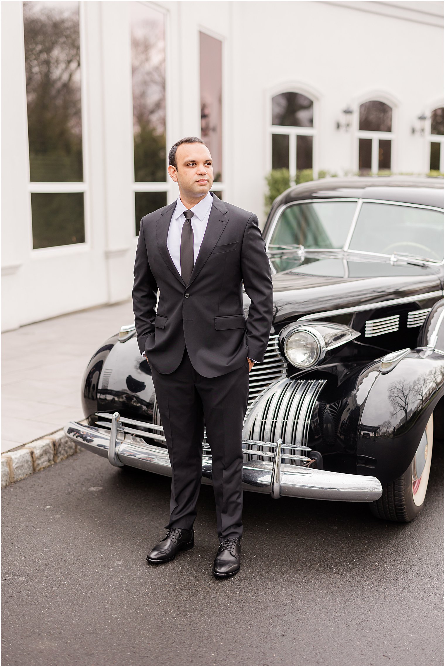 groom stands in front of classic black car at Mount Saint Mary Academy