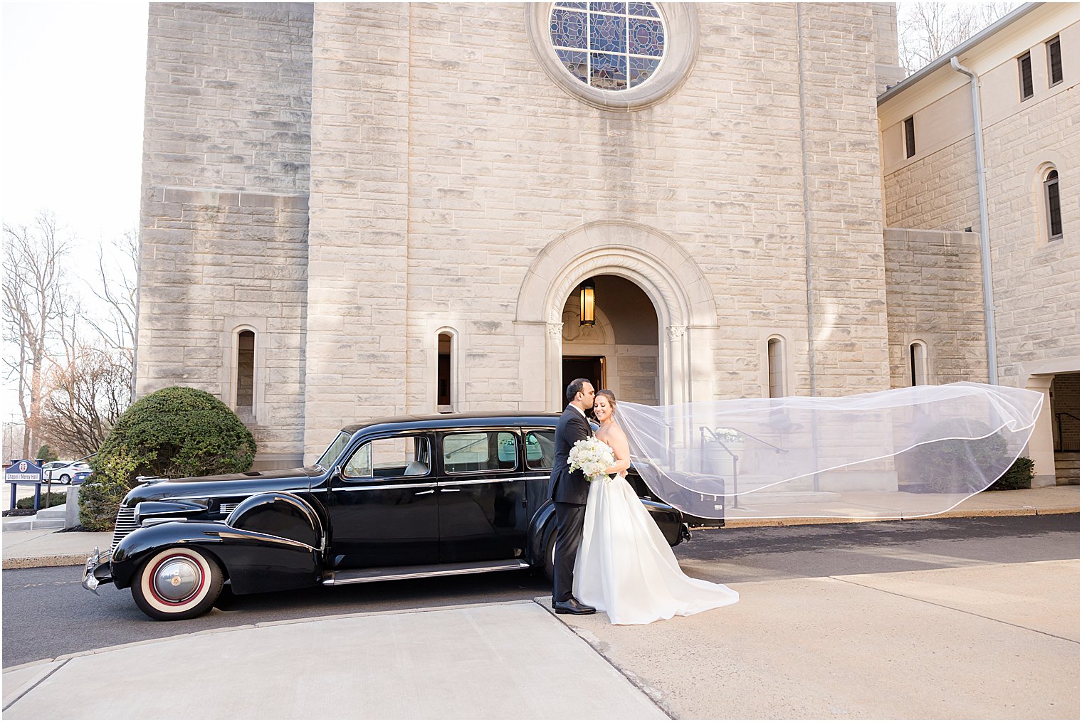 newlyweds kiss by classic black car outside the Immaculate Conception Chapel at Mount Saint Mary Academy