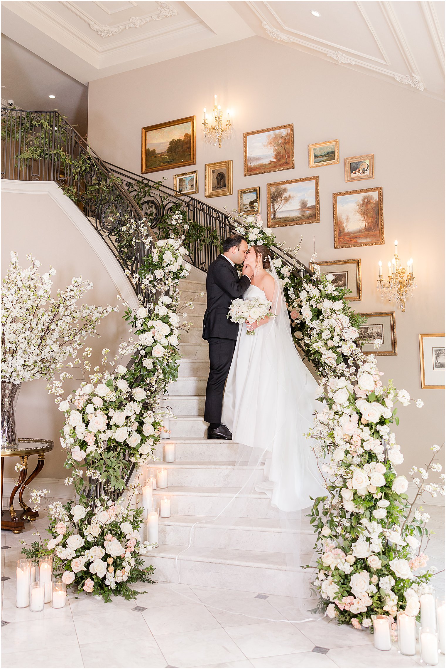 bride and groom stand on staircase with roses lining the railing 