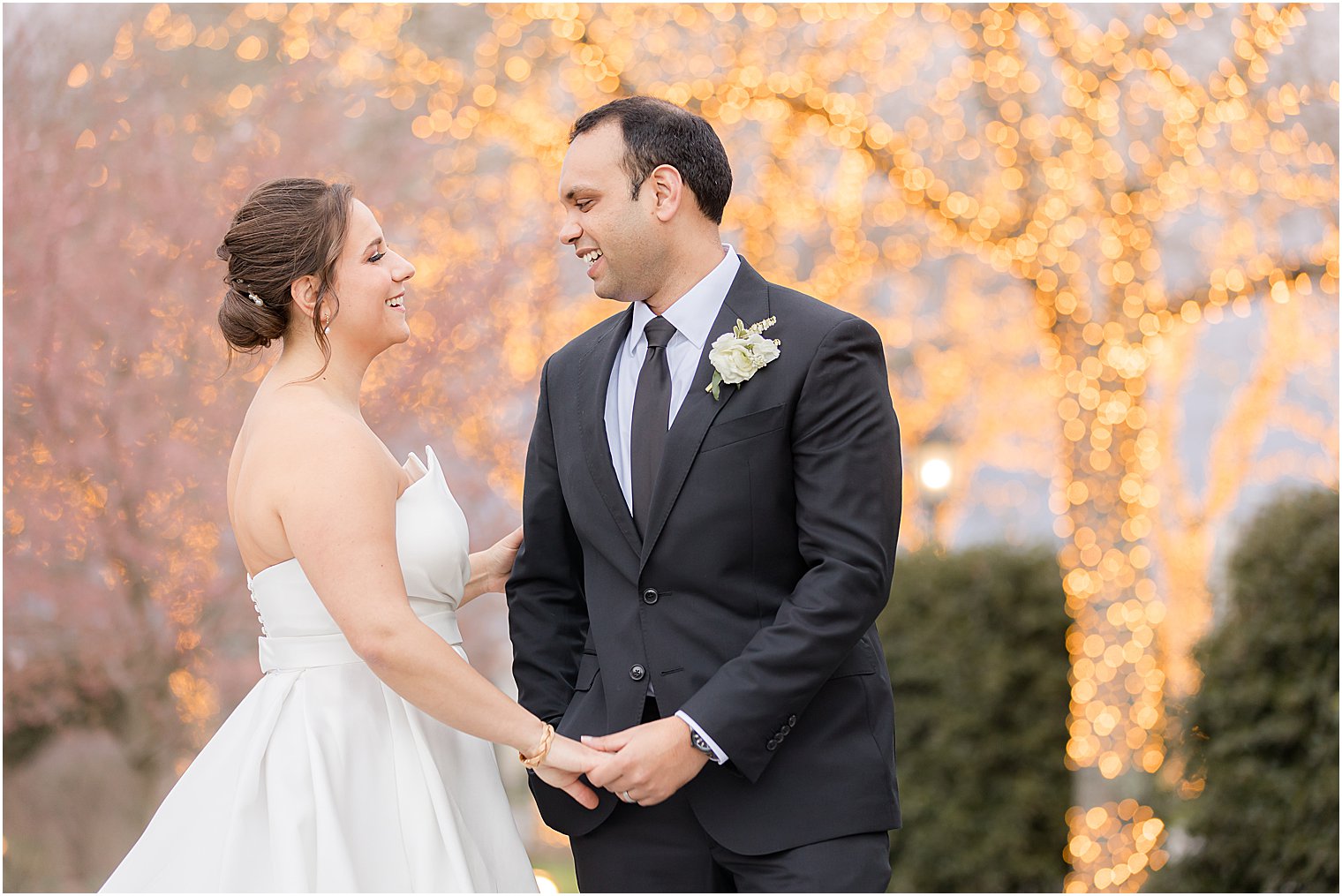 bride and groom smile together by tree with fairy lights at Park Chateau Estate