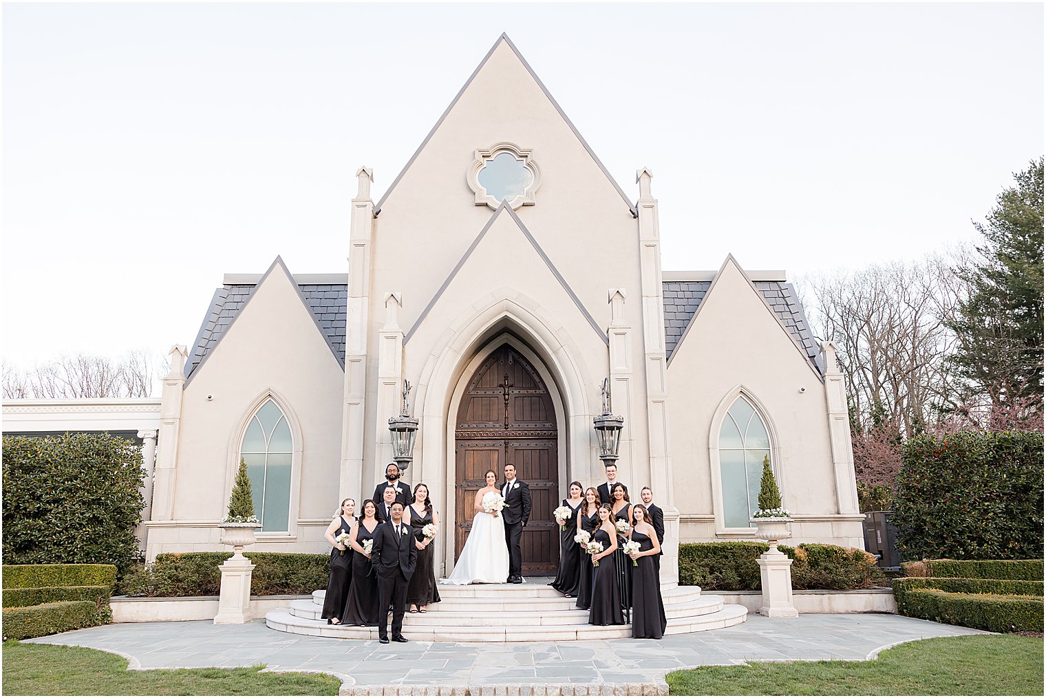 bride and groom stand on steps at Park Chateau Estate chapel with wedding party 