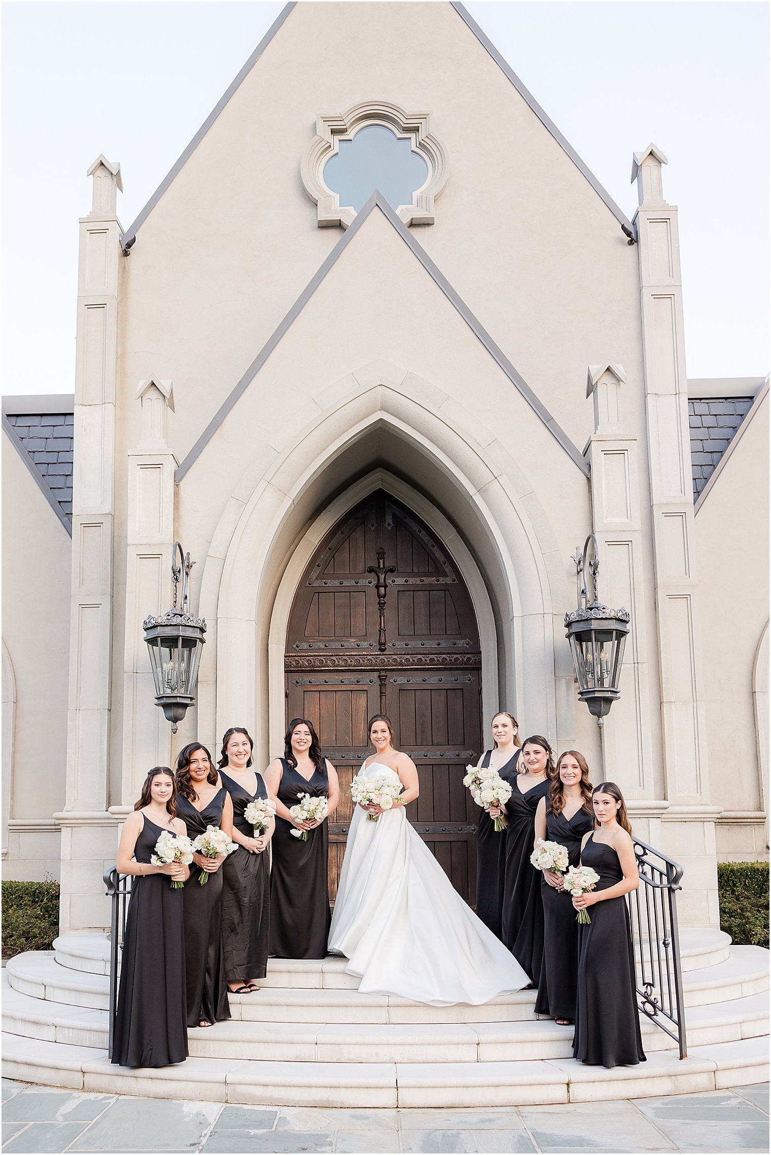 bride and bridesmaids in black gowns pose on Park Chateau Estate chapel steps 