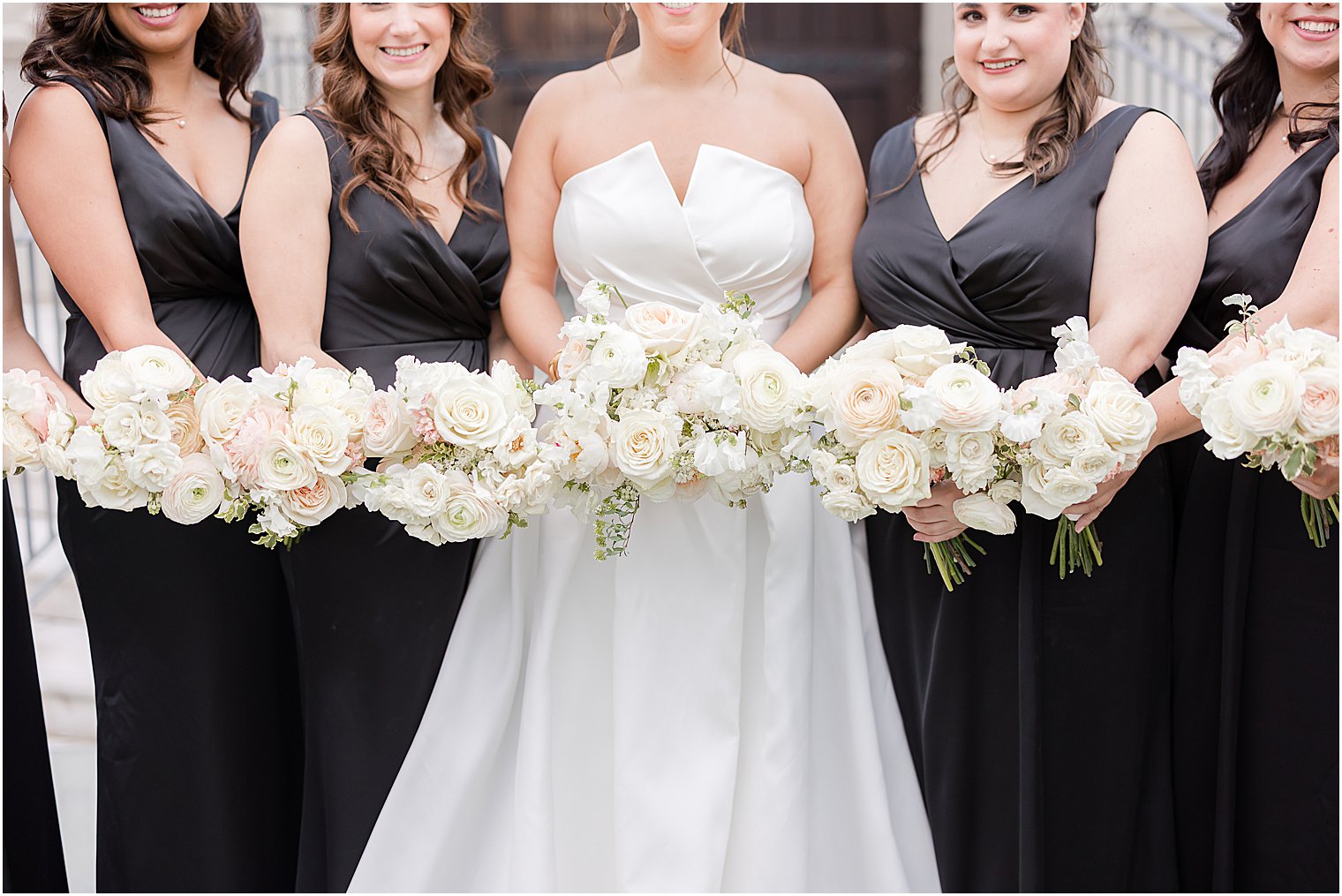 bride and bridesmaids hold bouquets of white roses 