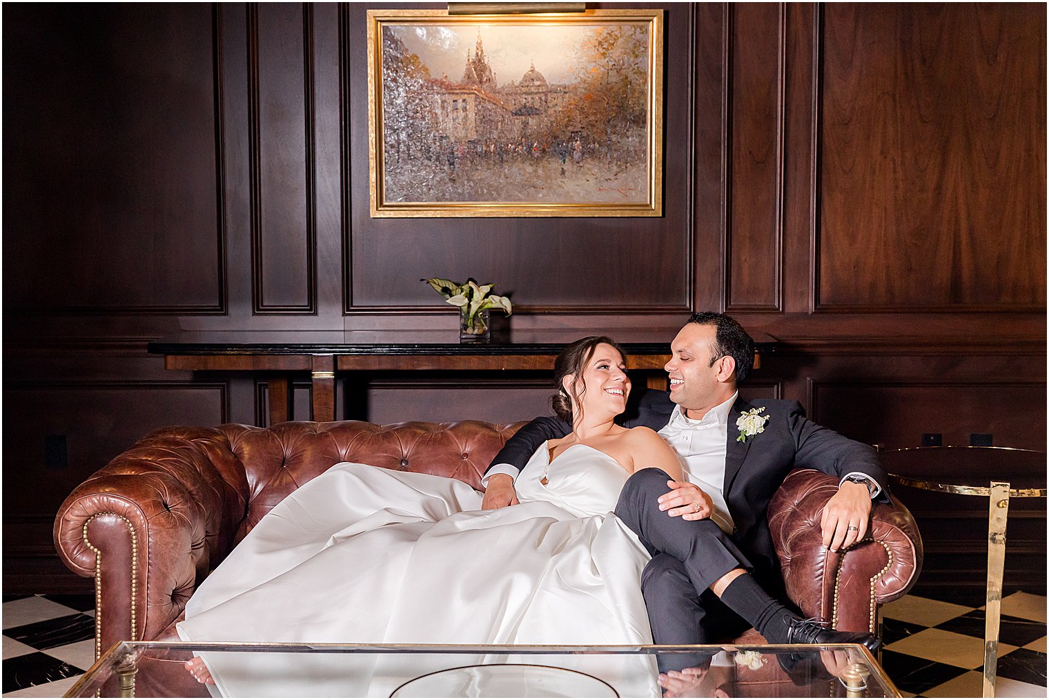 newlyweds sit on leather couch in library at Park Chateau Estate