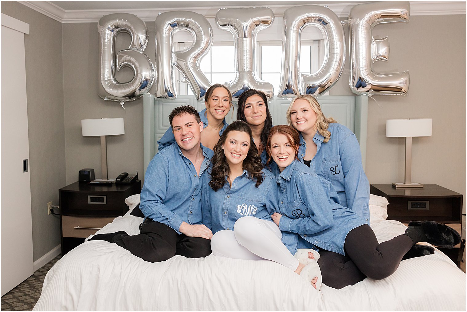 bride poses with bridesmaids in custom monogramed shirts under BRIDE balloons 