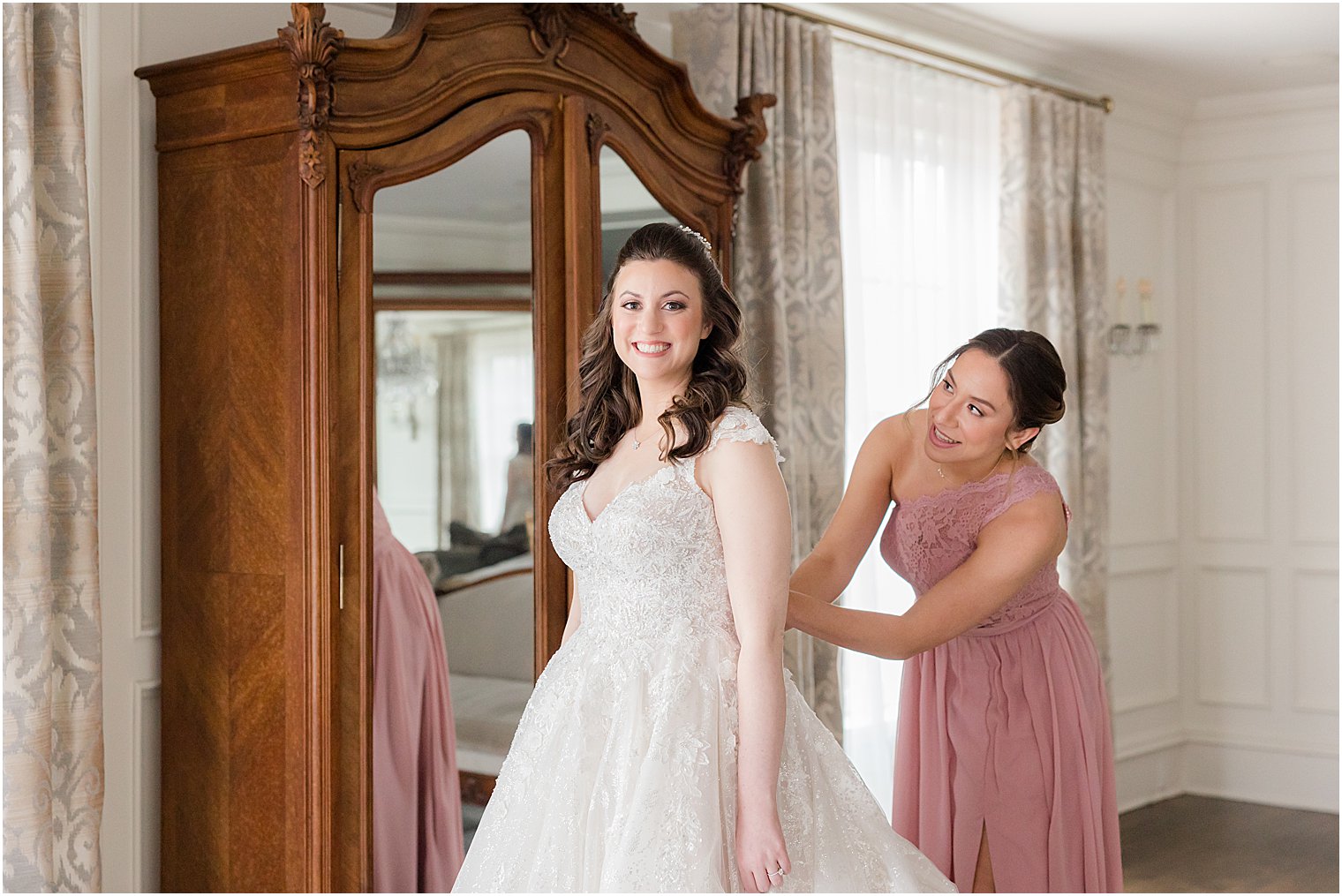 bridesmaid in pink gown helps bride into wedding dress