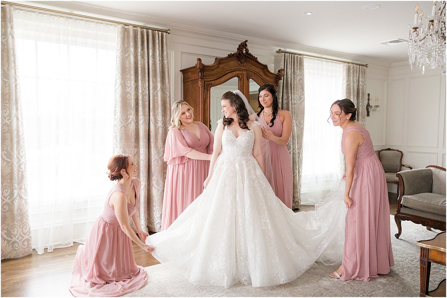 bridesmaids in pink gowns help bride with wedding dress