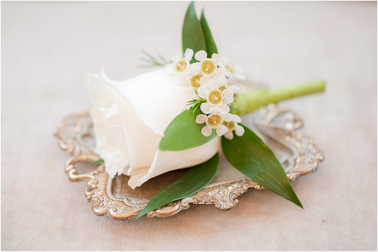 groom's white rose boutonnière on silver tray