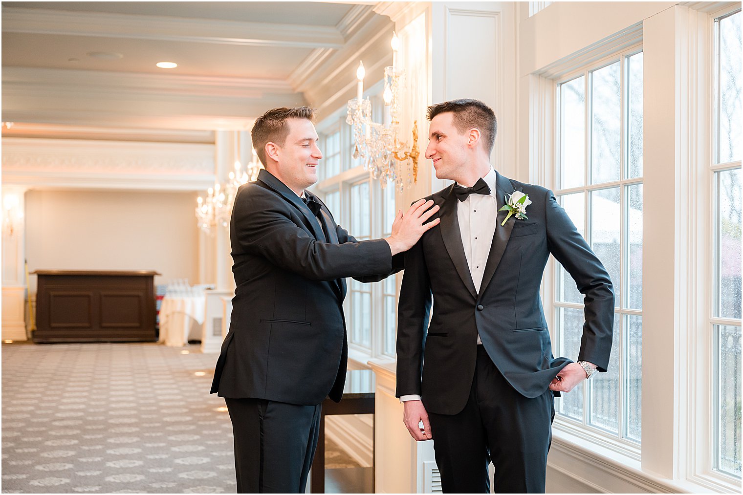groomsman helps groom with suit jacket 
