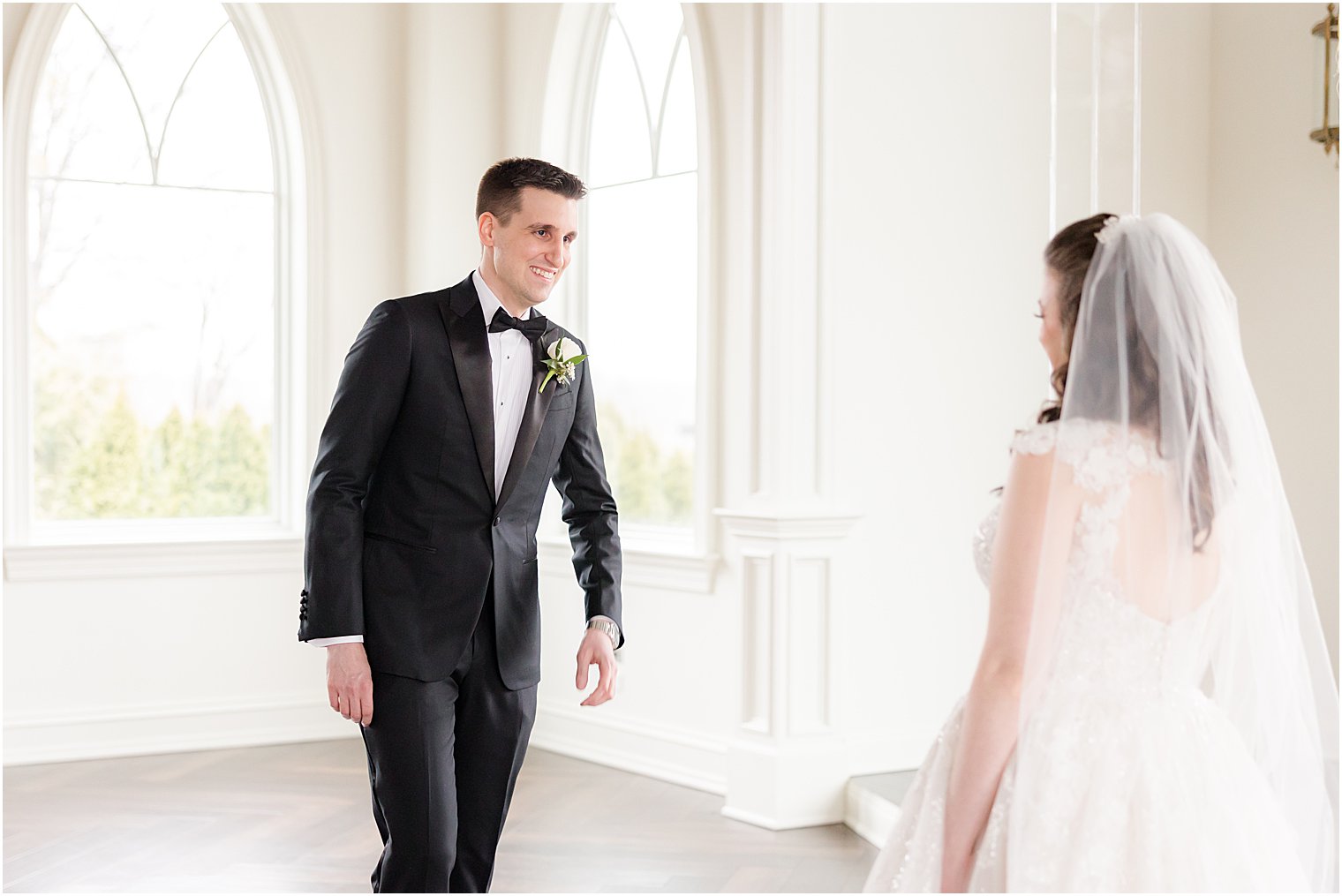 groom in black tux turns to see bride during first look smiling 