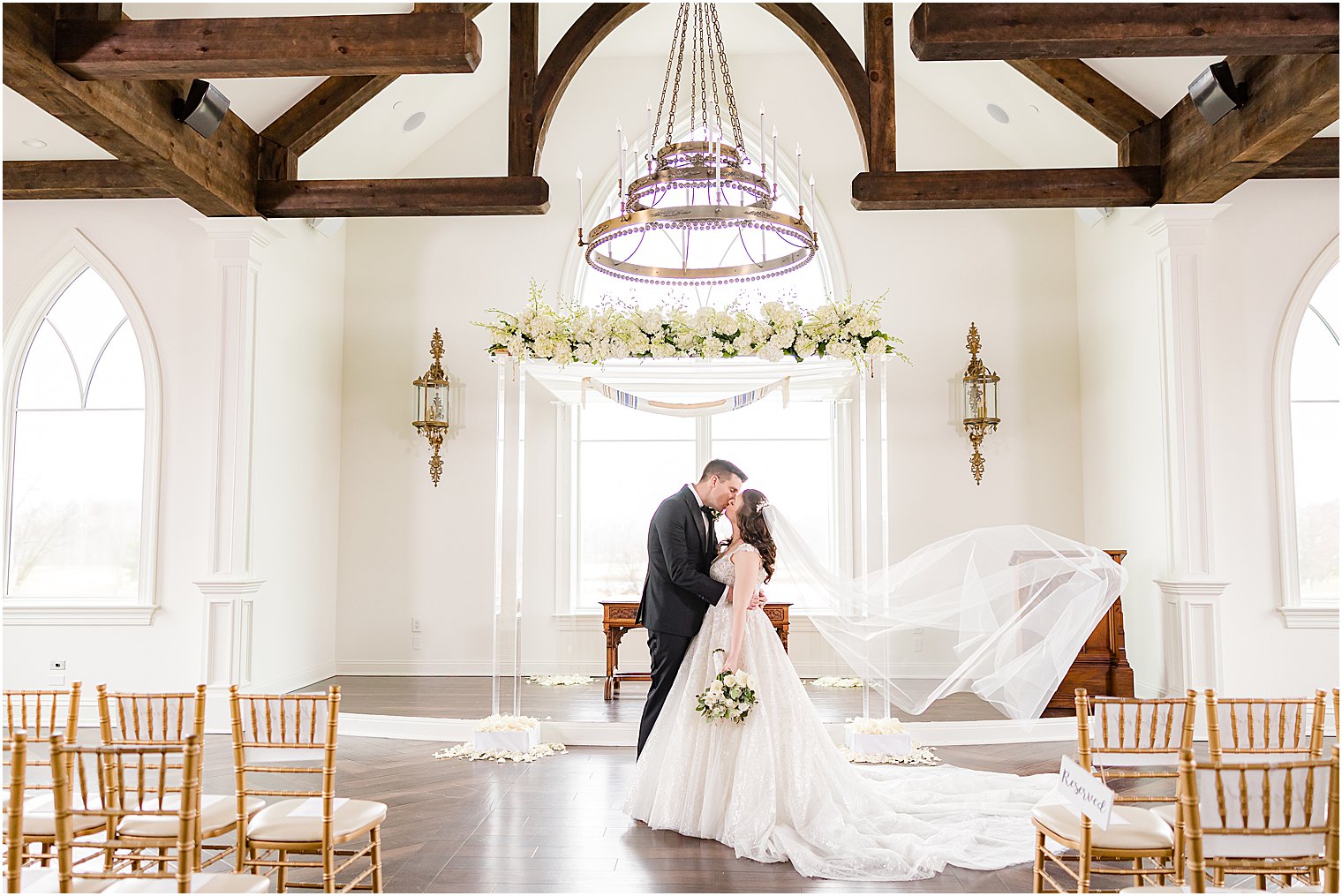 newlyweds kiss while bride's veil floats behind them near chuppah at Park Savoy Estate