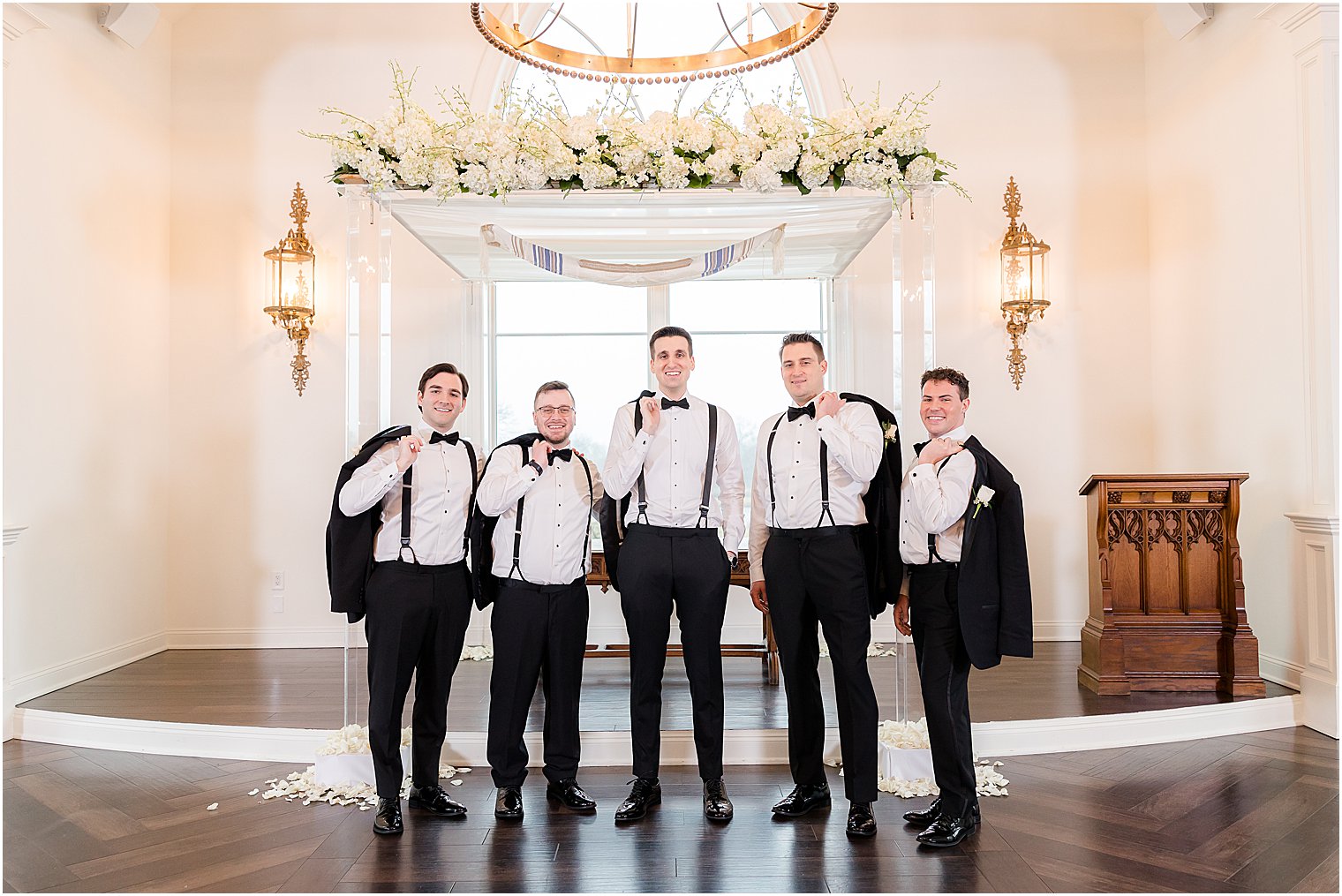 groom and groomsmen pose in chapel with jackets over their shoulders 