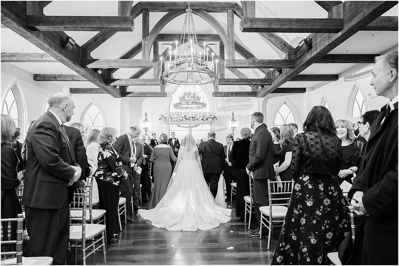 black and white portrait of bride walking down aisle with parents 