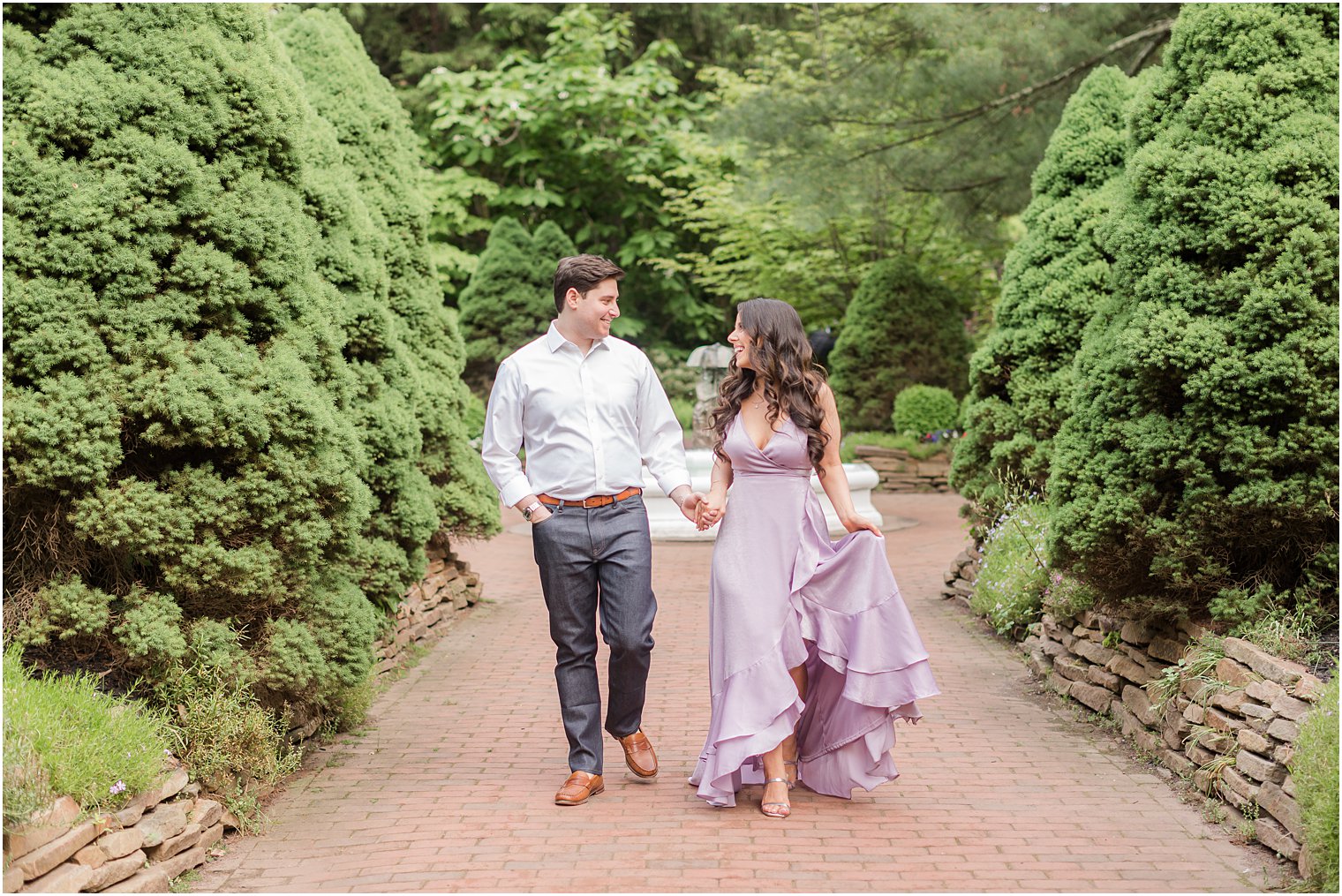 woman in purple dress moves skirt while walking with fiancee through Sayen Gardens 