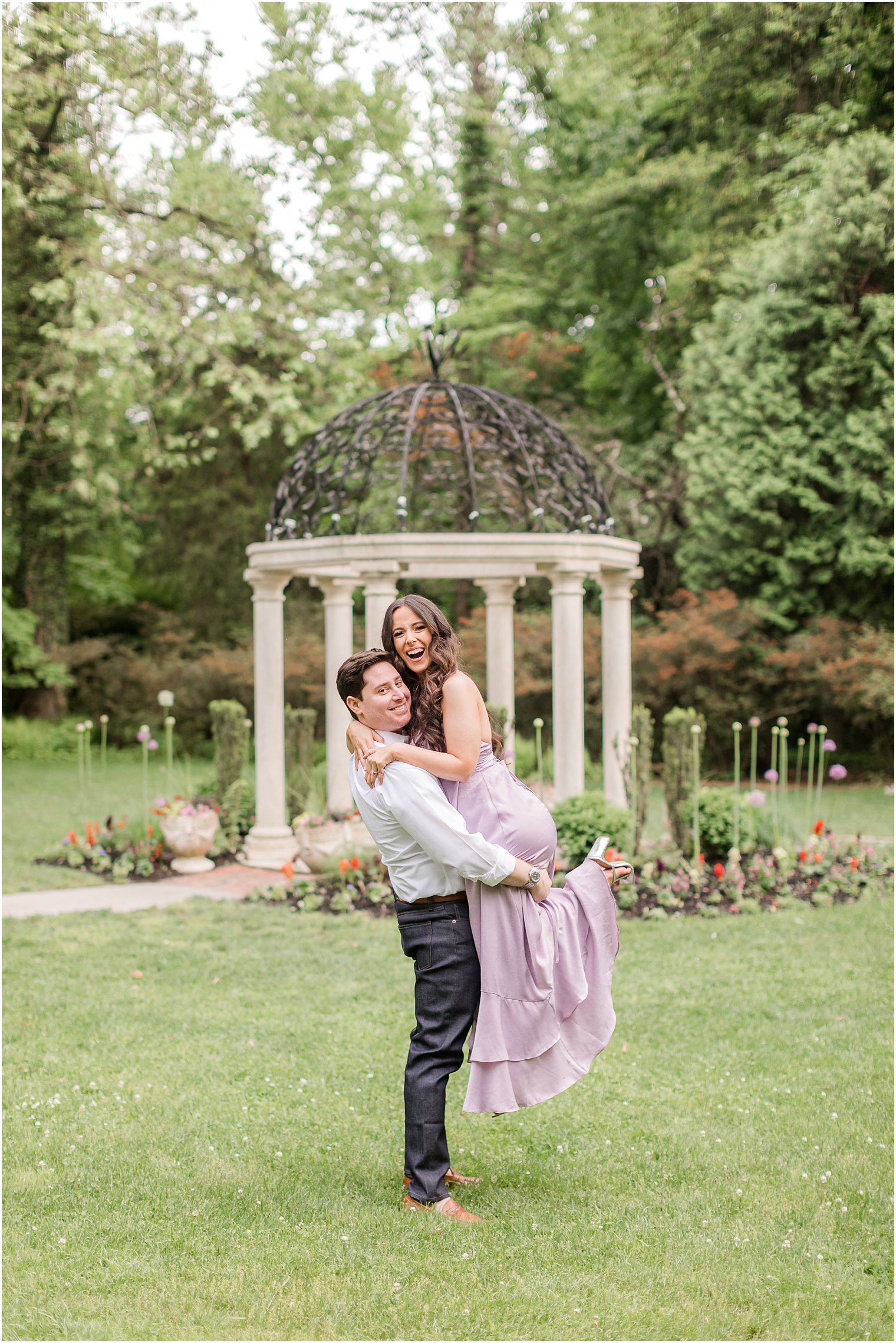man lifts woman in purple dress in front of gazebo at Sayen Gardens 