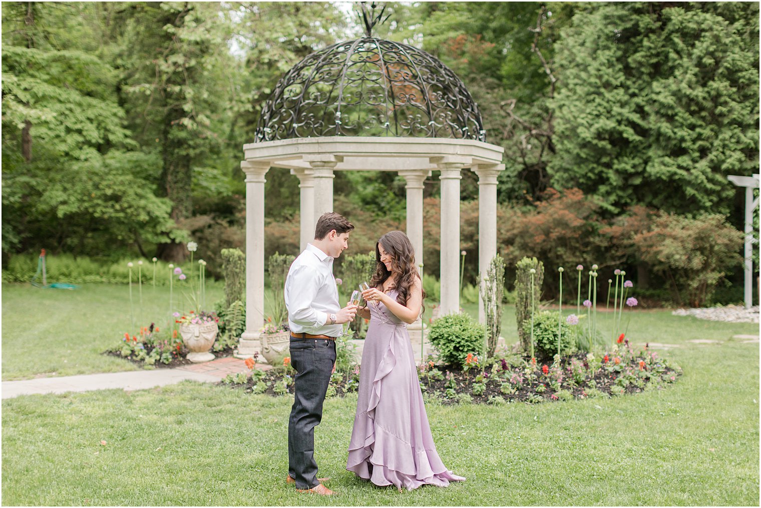 couple toasts champagne glasses in front of gazebo at Sayen Gardens 