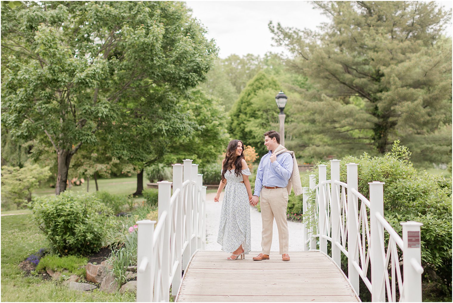 engaged couple holds hands walking on wooden bridge at Sayen Gardens 