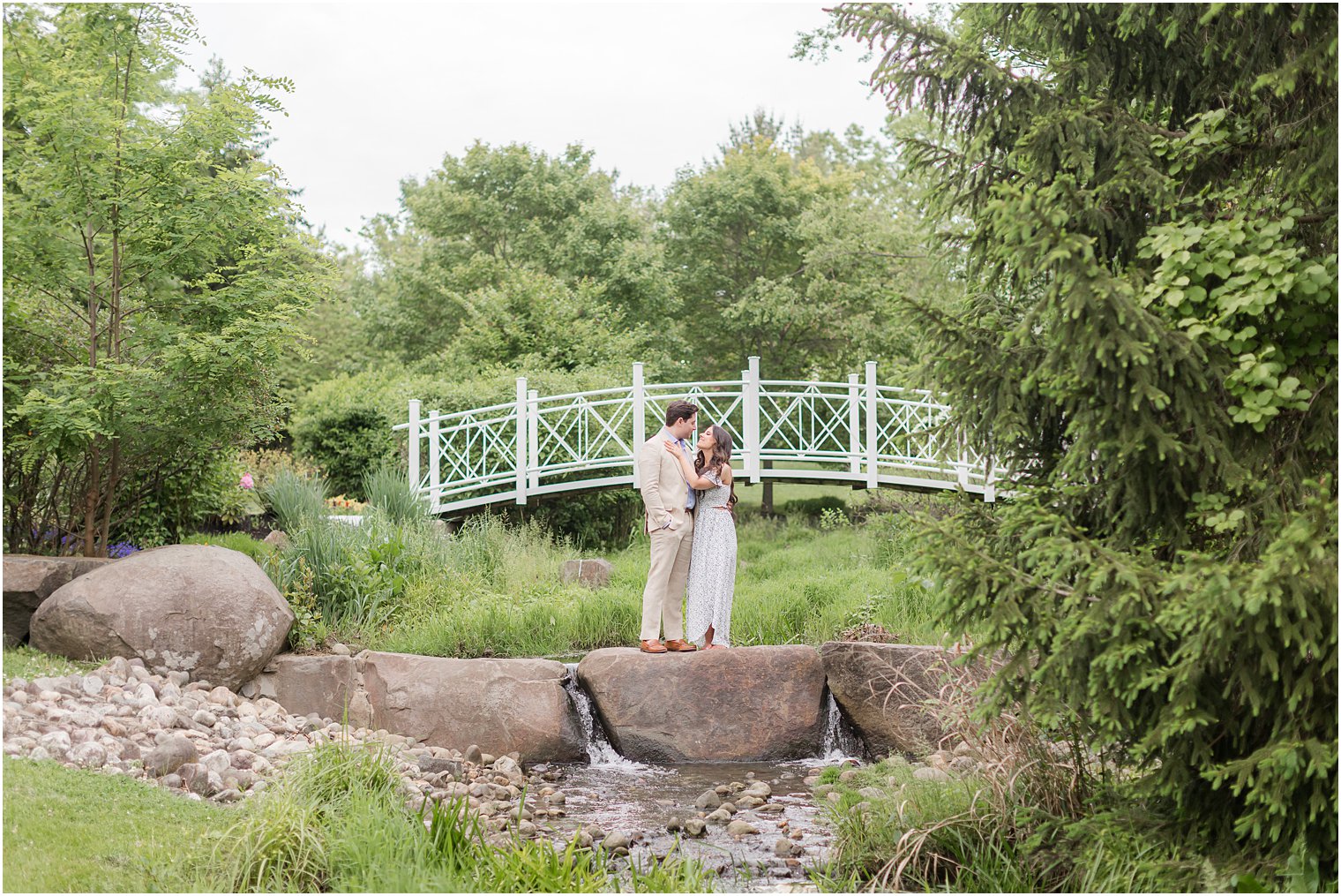couple kisses on rocks by bridge in Sayen Gardens 