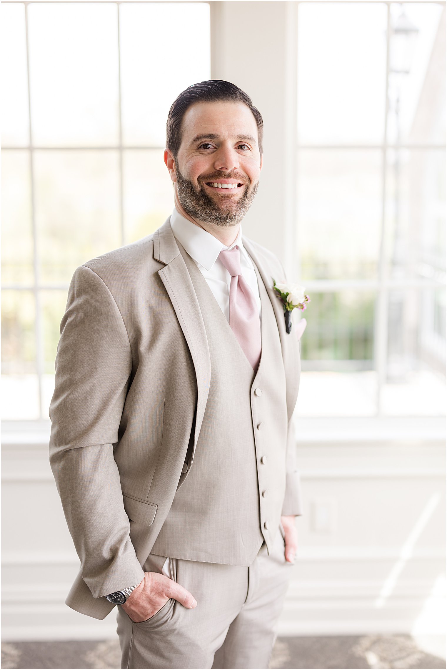 groom stands with hands in pocket in tan suit with pink tie for spring wedding at Park Savoy Estate