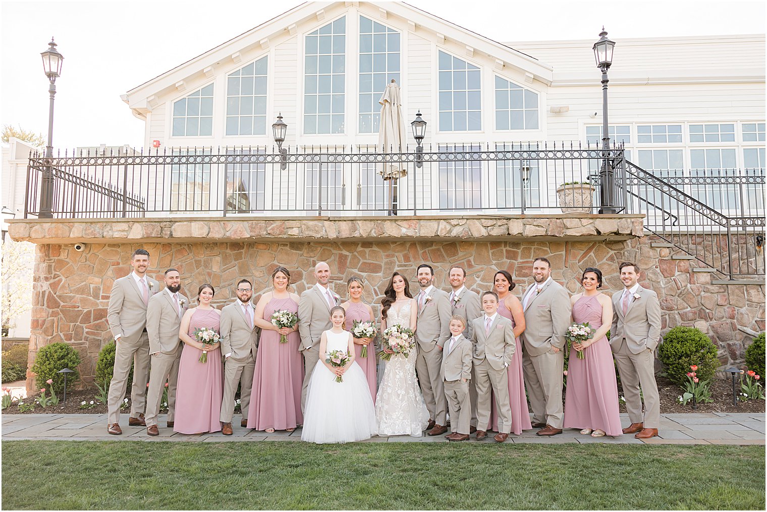 bridesmaids in pink gowns with groomsmen in tan suits pose outside Park Savoy Estate with newlyweds 