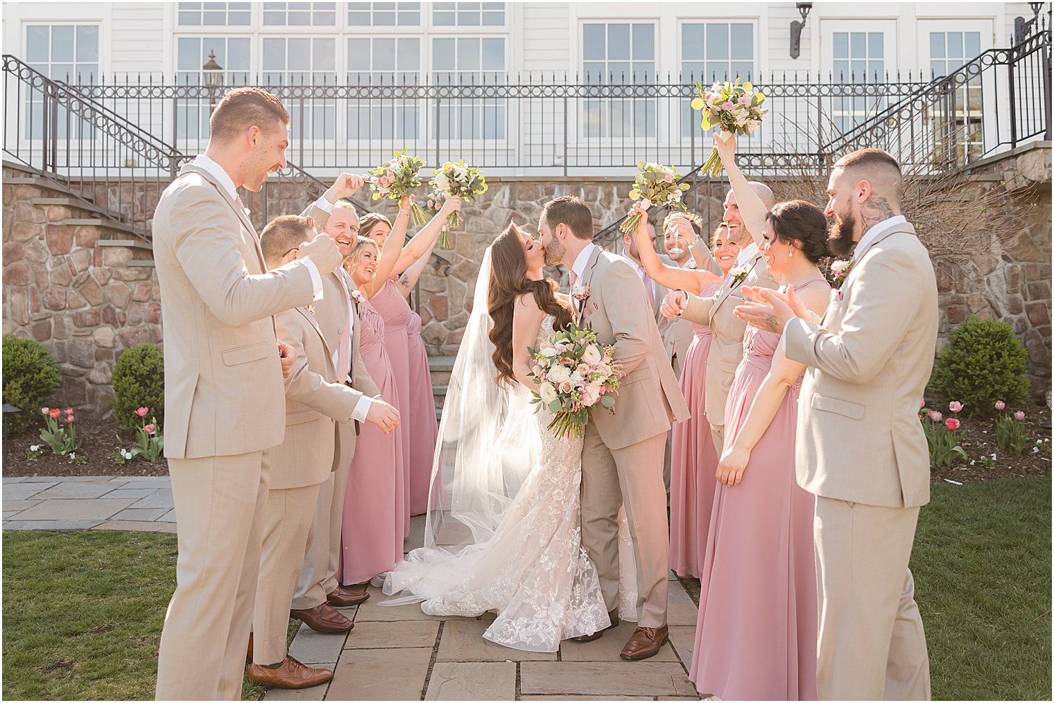 bride and groom kiss with bridal party holding bouquets in air 