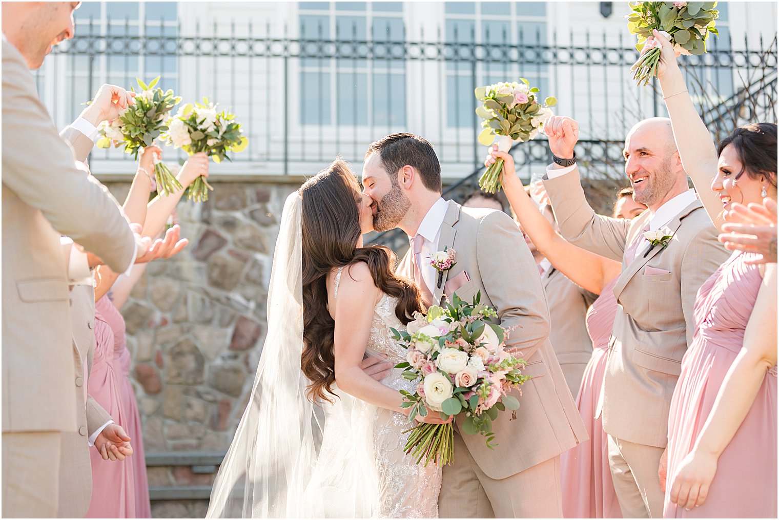 newlyweds kiss with bridal party cheering behind them 