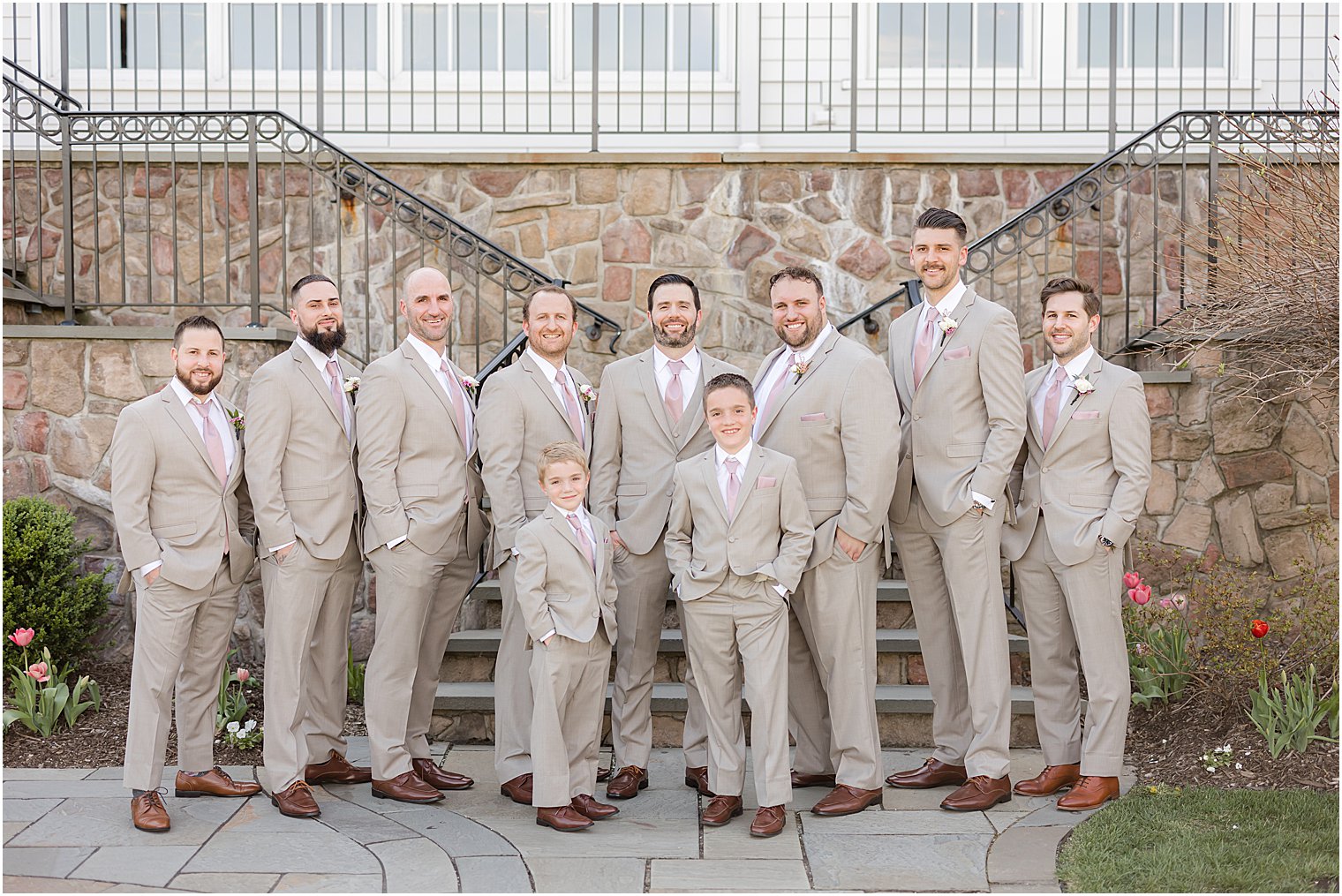 groom stands behind Park Savoy Estate with groom and groomsmen in tan suits