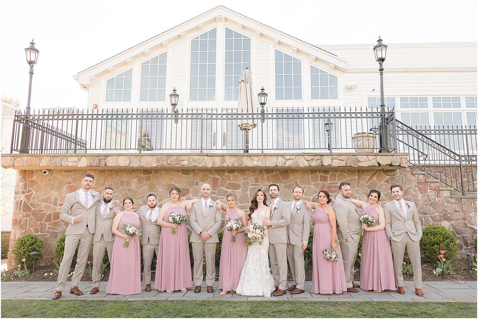 bride and groom pose with bridesmaids in pink gowns and groomsmen in tan suits 