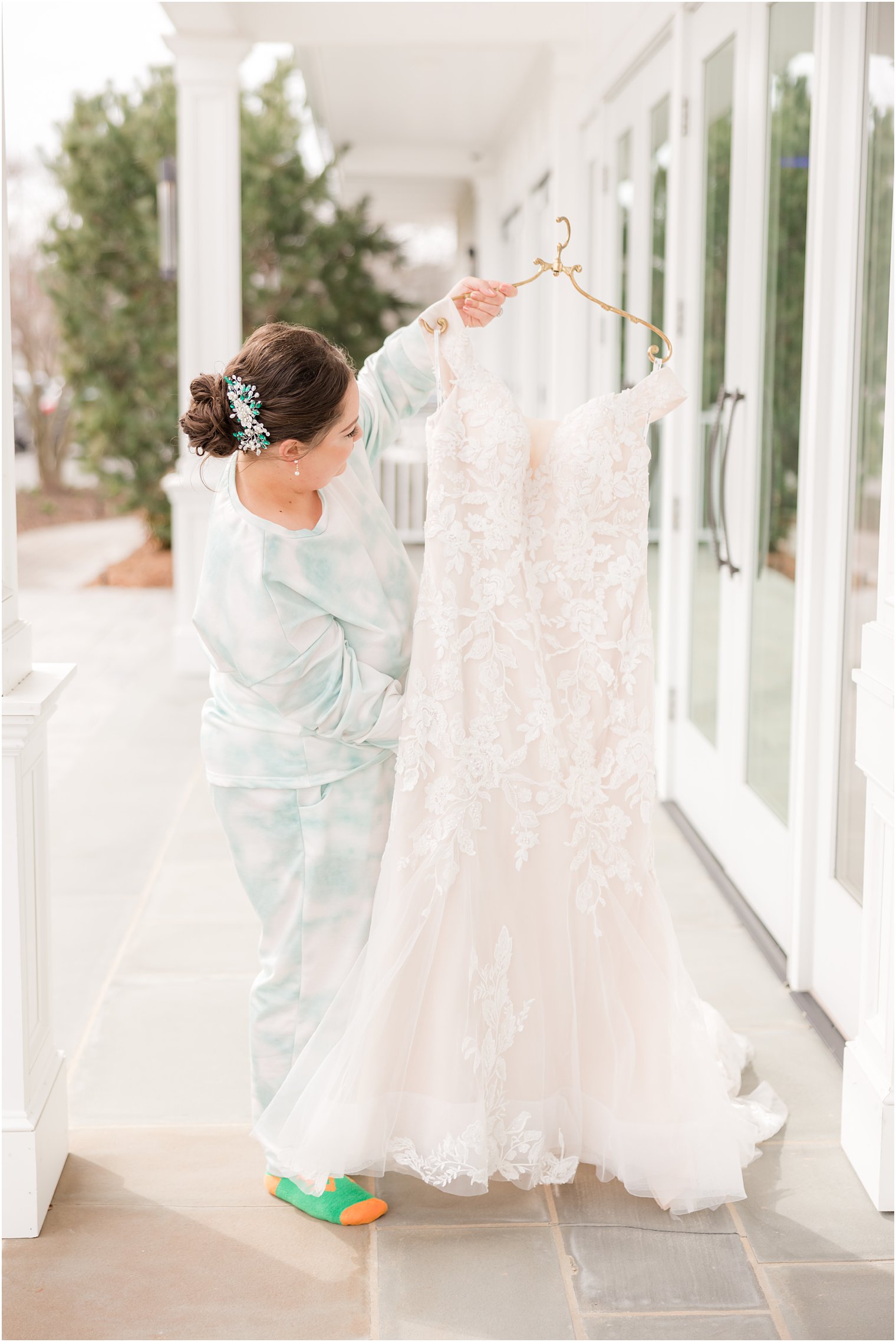 bride in green and white pajamas looks at wedding dress on balcony at Crystal Point Yacht Club