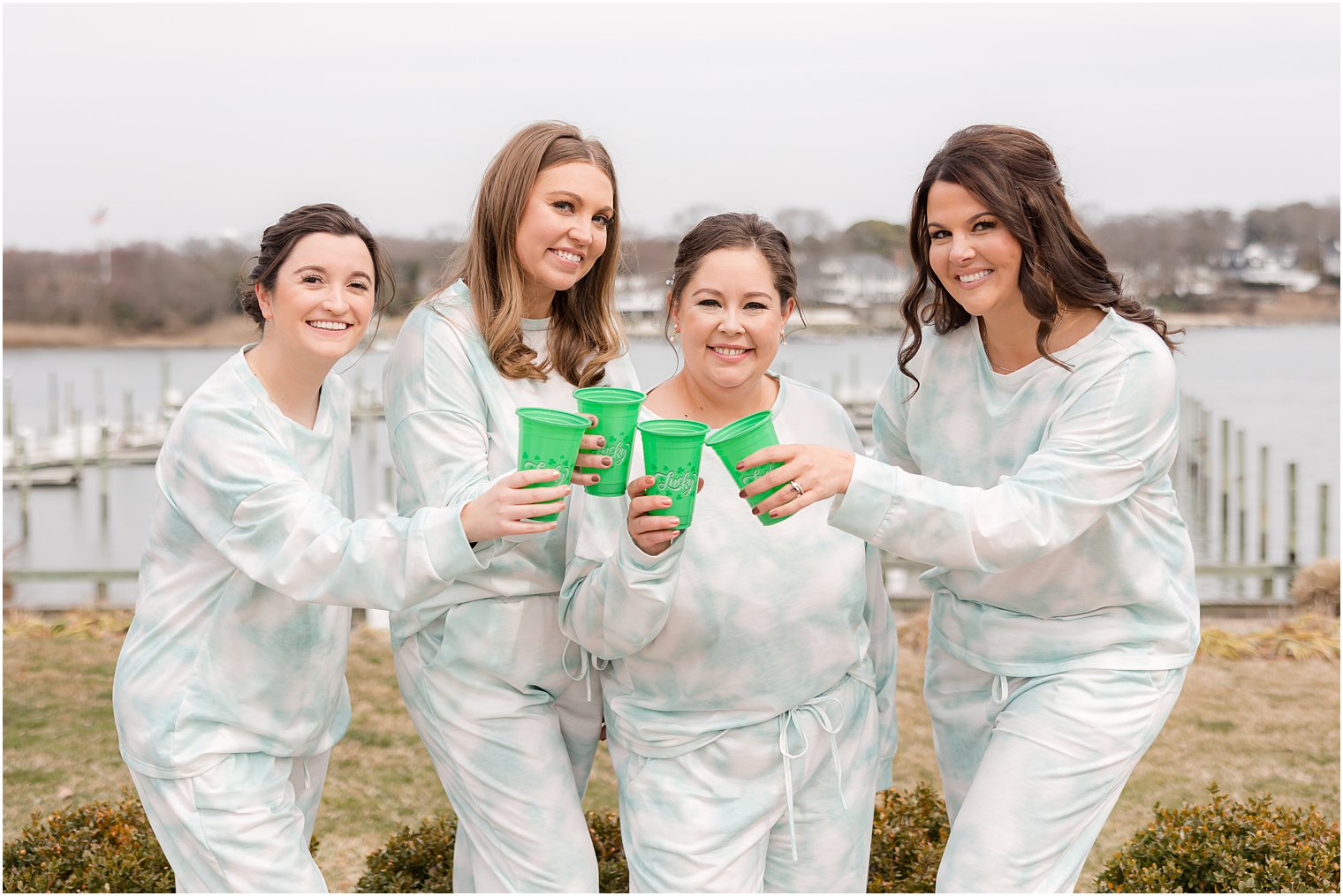 bridesmaids hold green cups with bride on balcony at Crystal Point Yacht Club