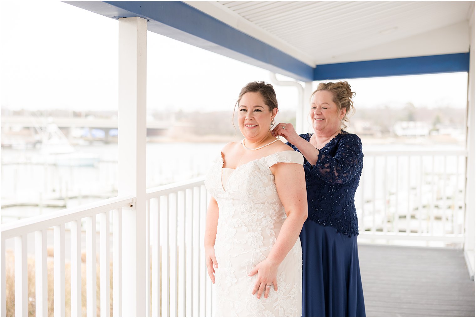 mother helps bride with pearl earrings on balcony at Crystal Point Yacht Club
