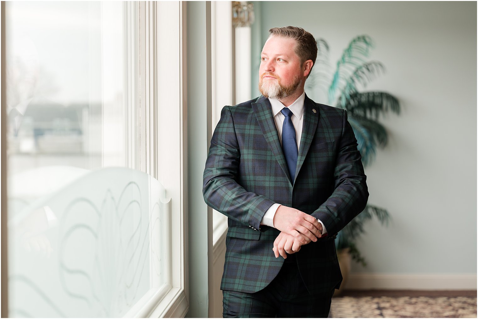 groom stands looking out window at Crystal Point Yacht Club