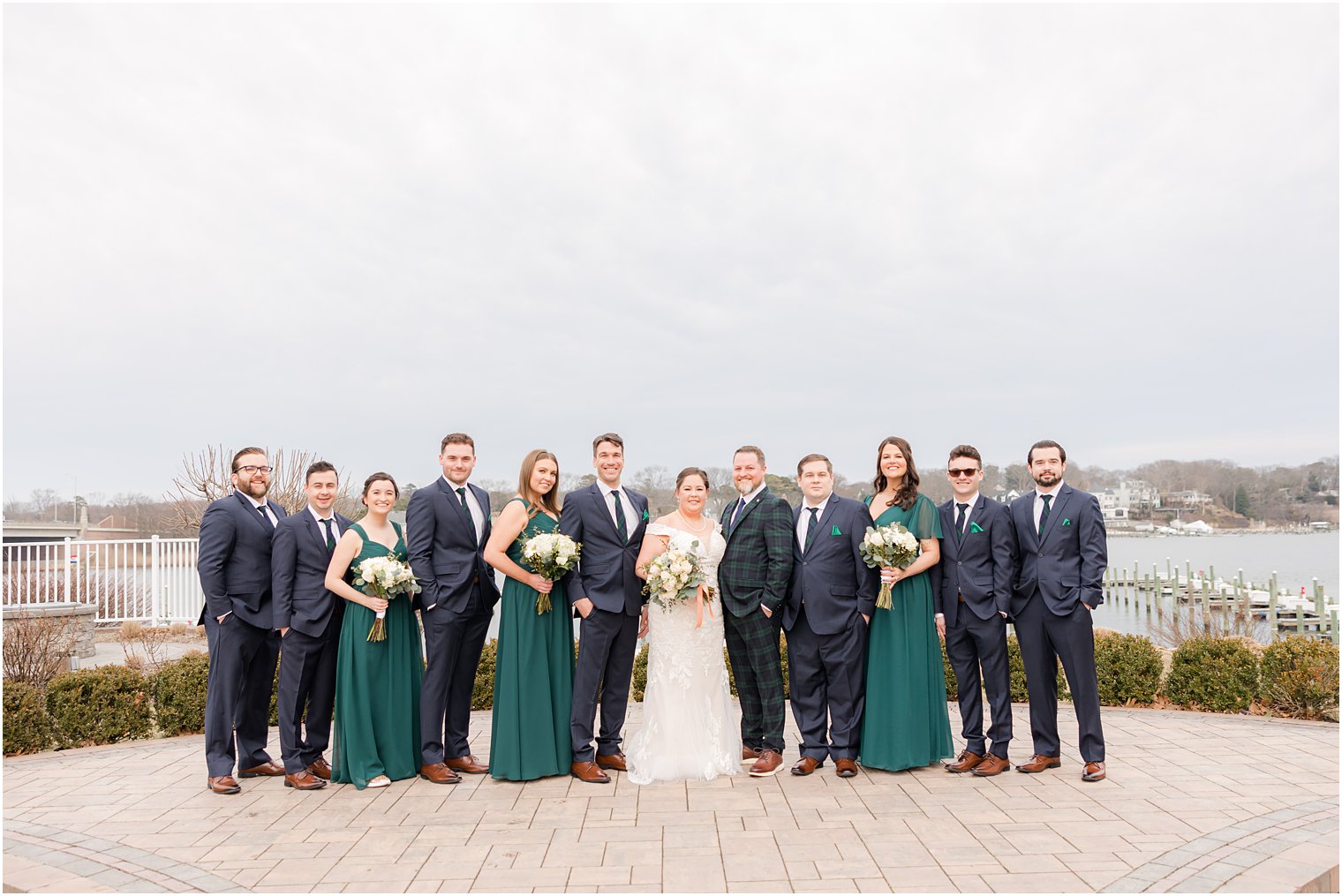 bride and groom stand with wedding party in teal gowns and plaid suits