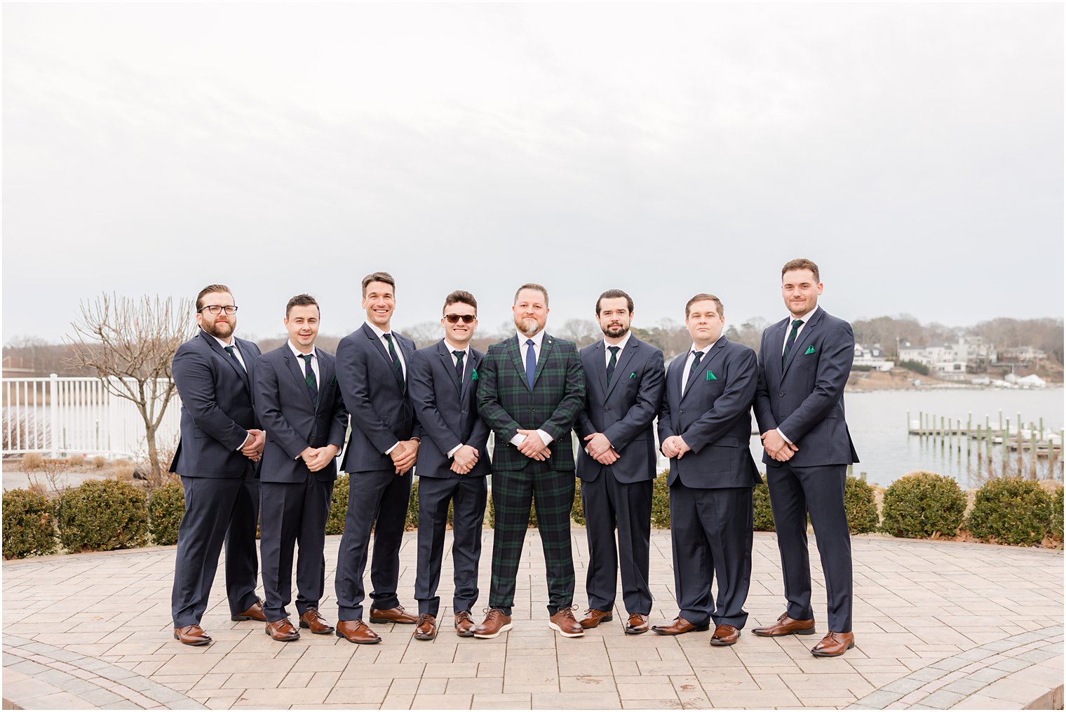 groom stands with groomsmen in plaid suits on patio at Crystal Point Yacht Club