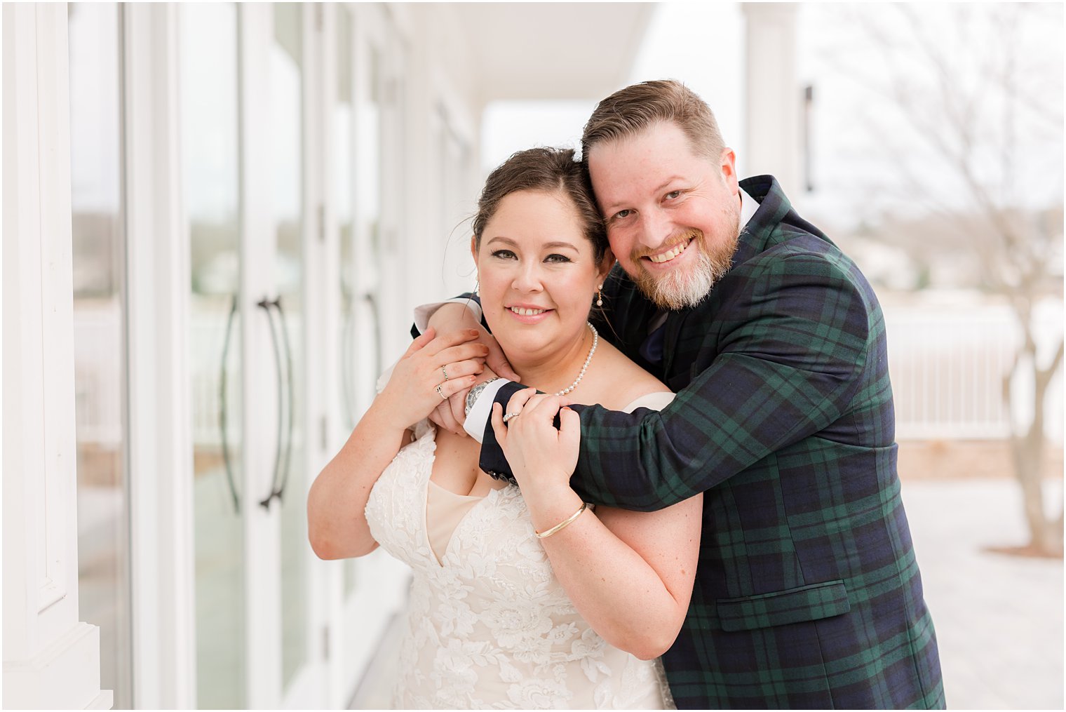 groom in plaid suit hugs bride from behind at Crystal Point Yacht Club