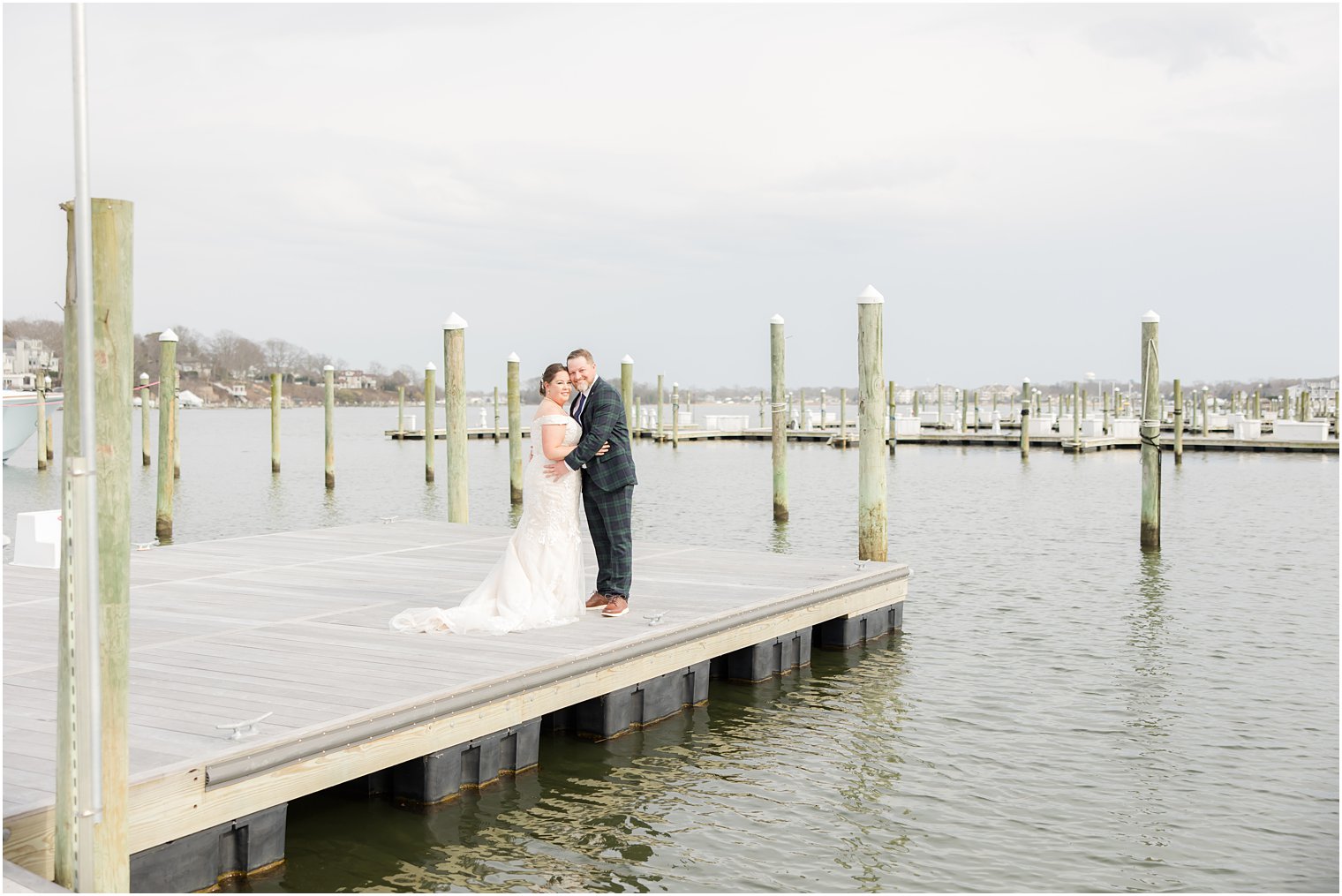 bride and groom hug on pier in New Jersey 