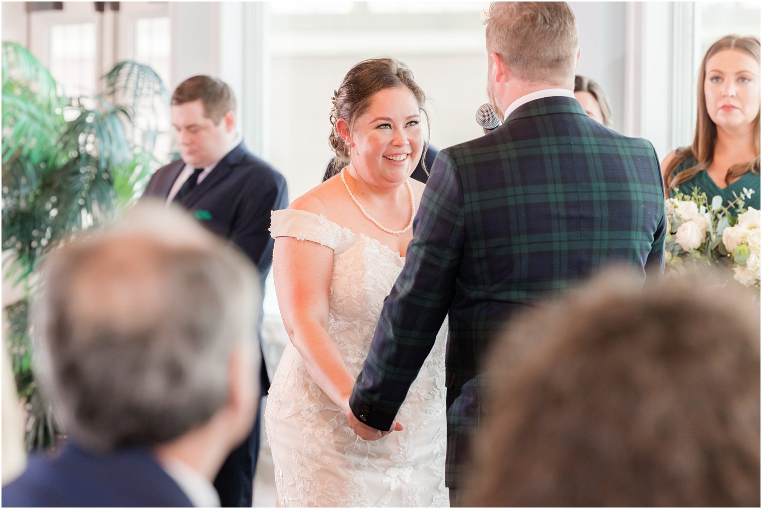 bride holds groom's hand smiling during wedding ceremony with waterfront views at Crystal Point Yacht Club